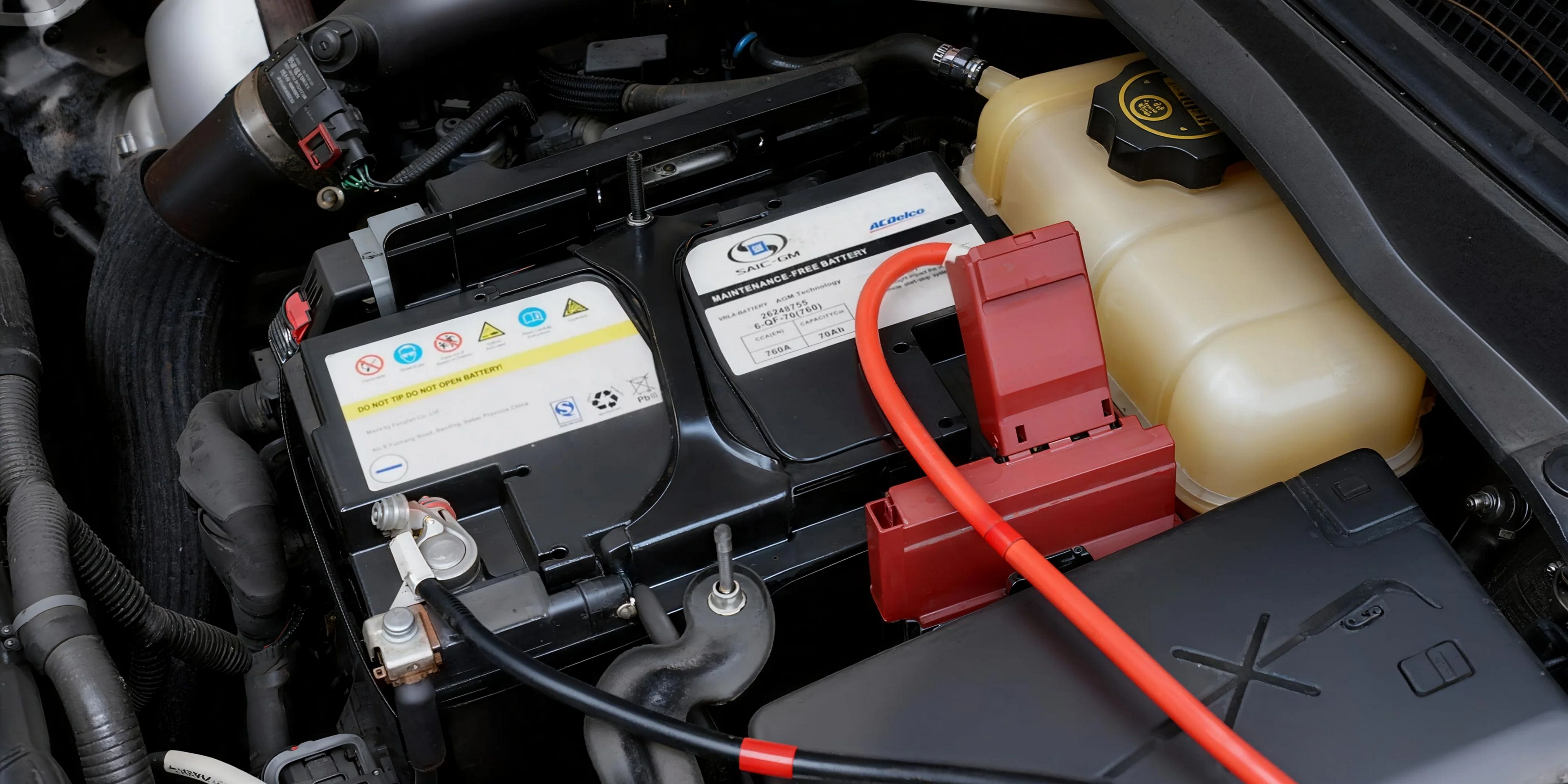 Akumulator samochodowy z czerwonym kablem rozruchowym i zbiornikiem płynu chłodzącego.