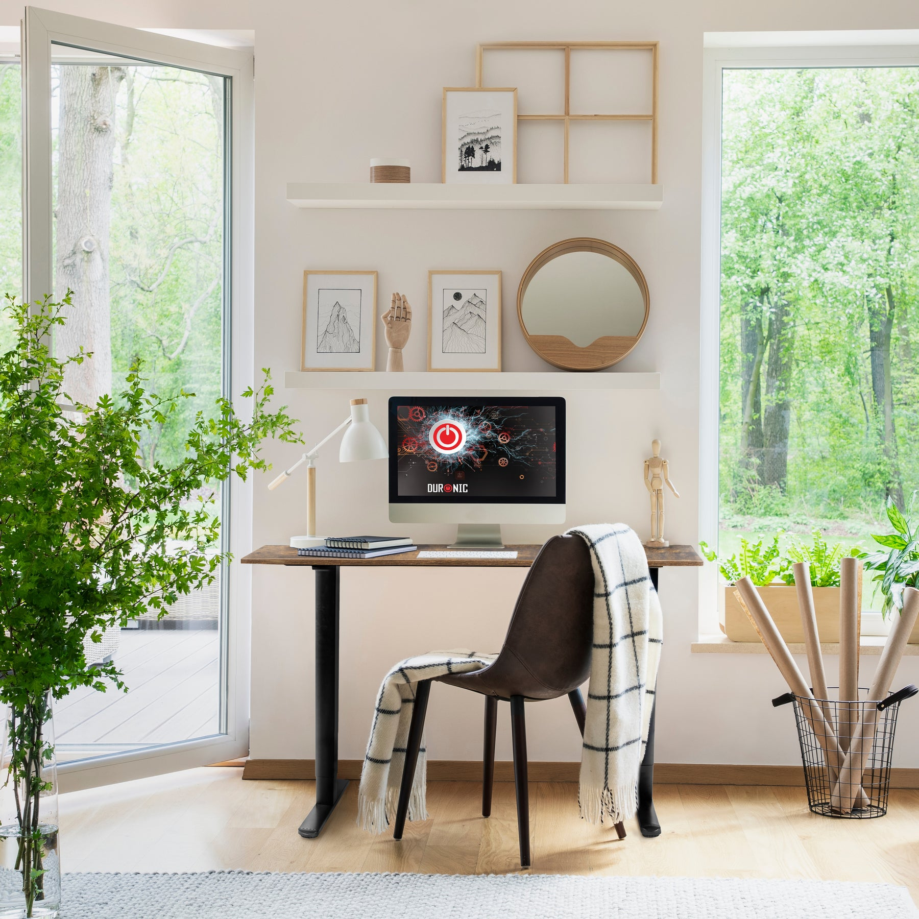 Ein Schreibtisch mit Computer, Lampe, Stuhl und Pflanze vor einem offenen Fenster mit Bäumen.
