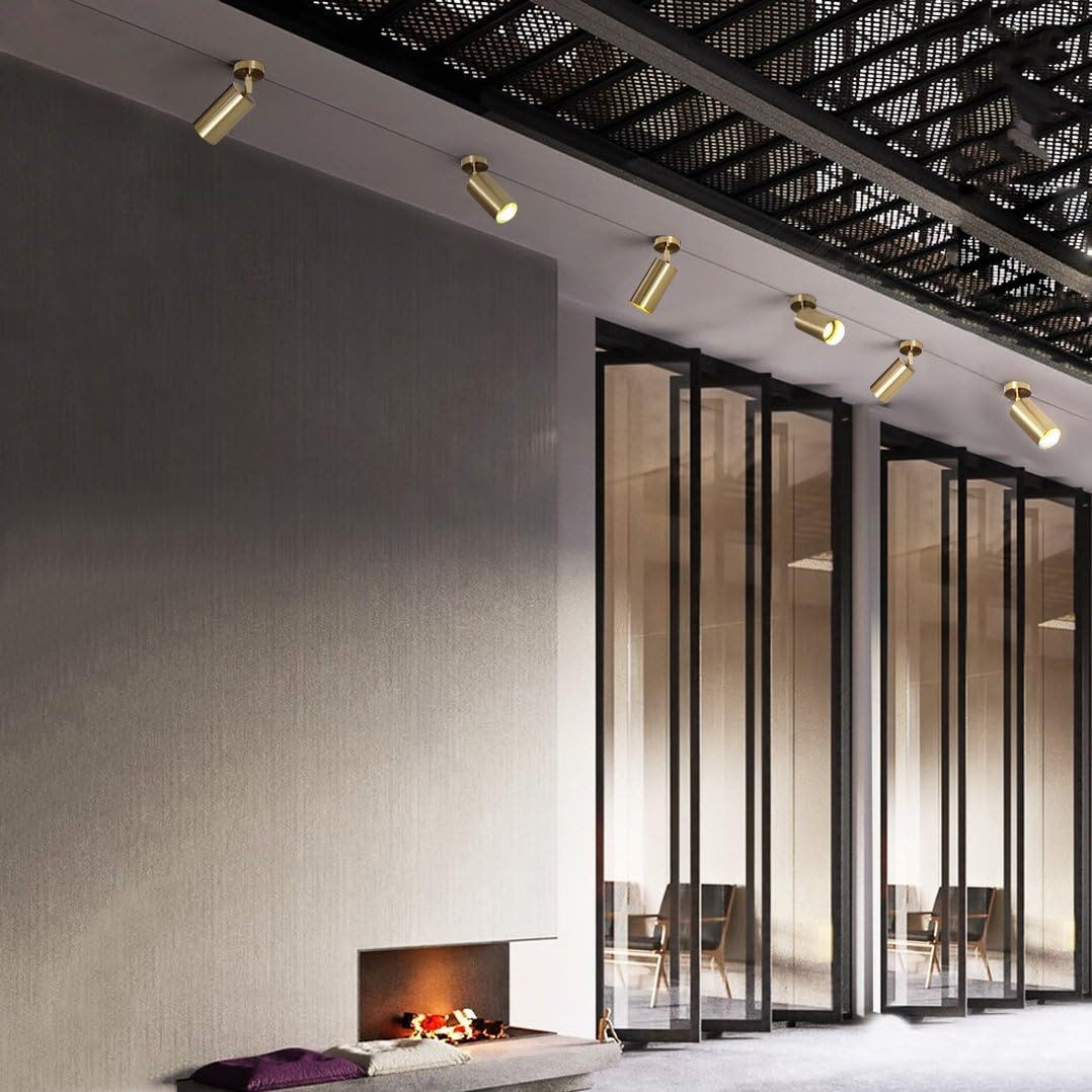 Mosiężne reflektory oświetlają ścianę z kominkiem i szklanymi panelami.