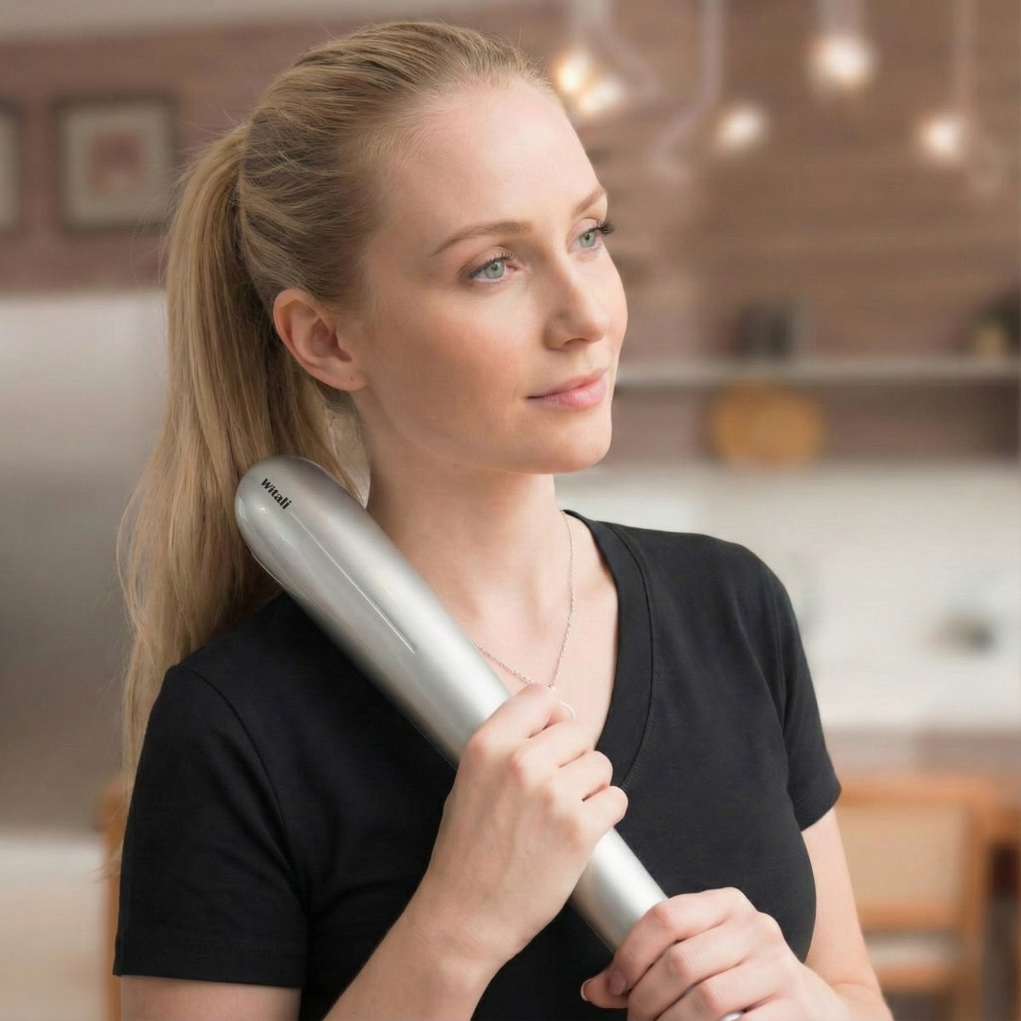 Blonde Frau im schwarzen Hemd hält silbernes Massagegerät. Verschwommener Hintergrund.