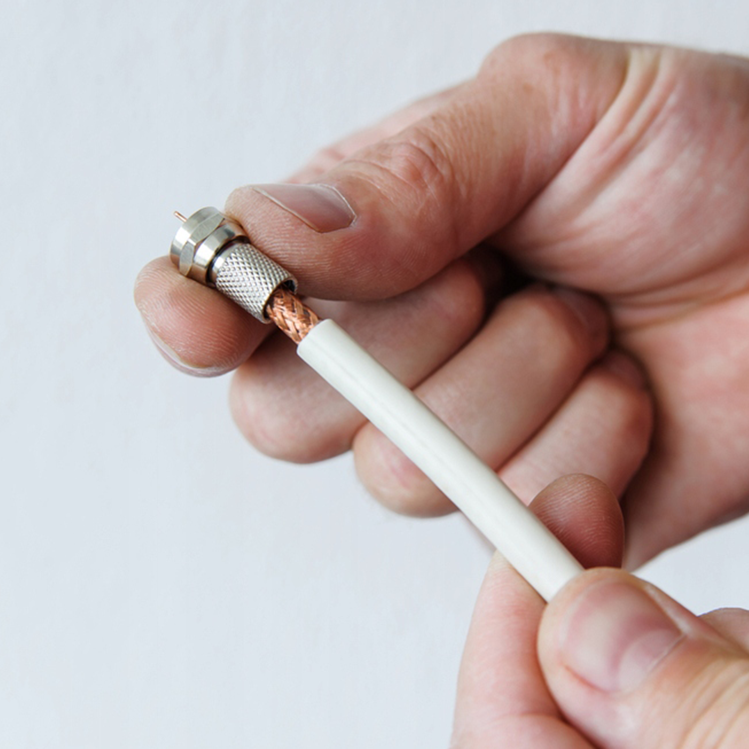 Dłonie montujące złącze kabla koncentrycznego z miedzianymi przewodami i białą osłoną.