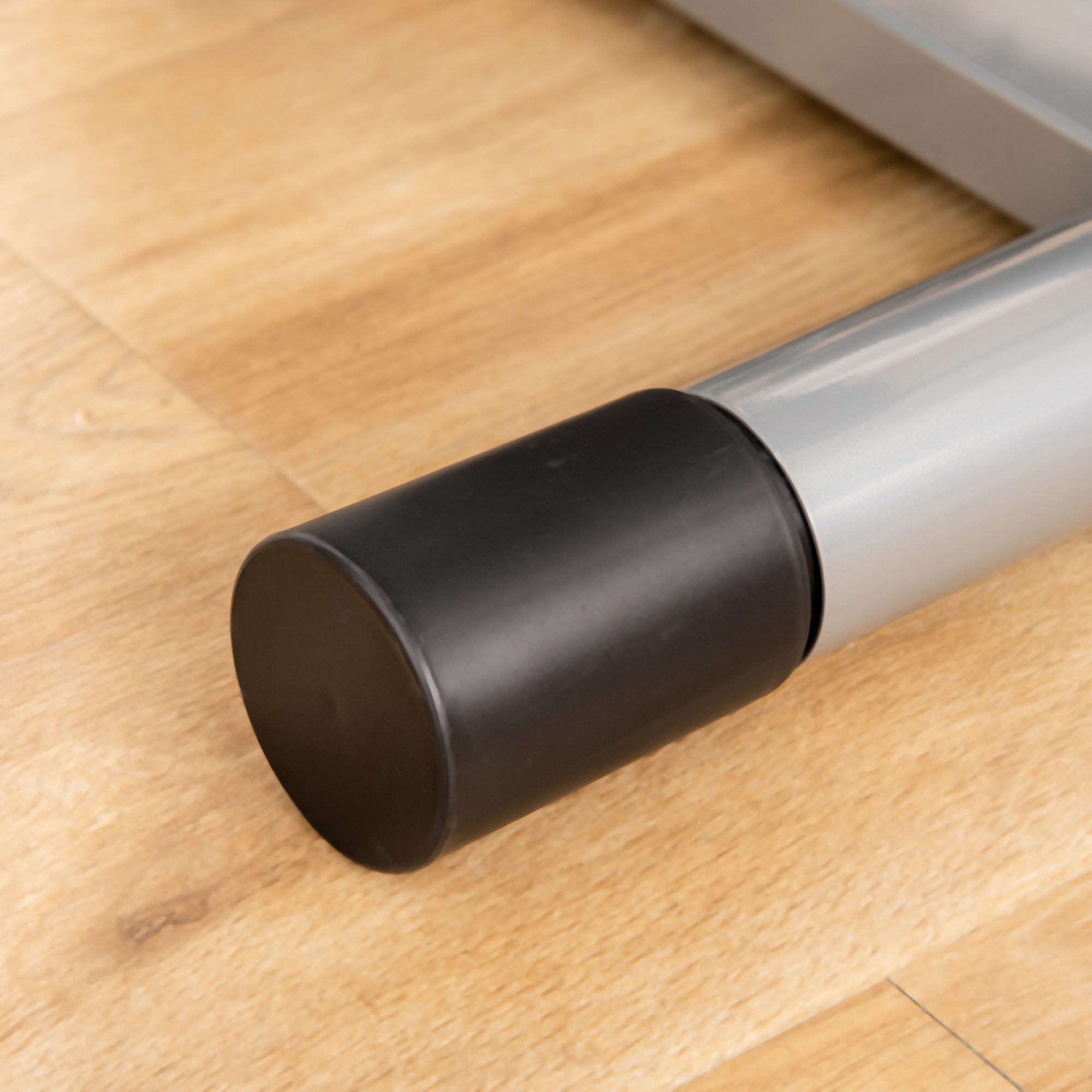 Czarna gumowa stopka na srebrnej metalowej rurze na drewnianej podłodze.
