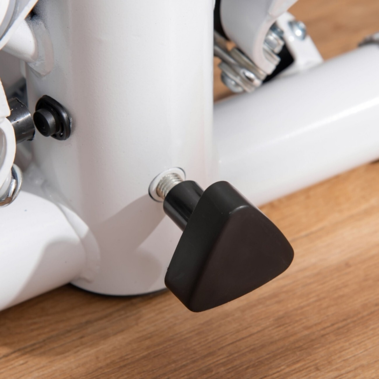 Zbliżenie czarnego pokrętła na białej metalowej ramie, stojącej na drewnianej podłodze.