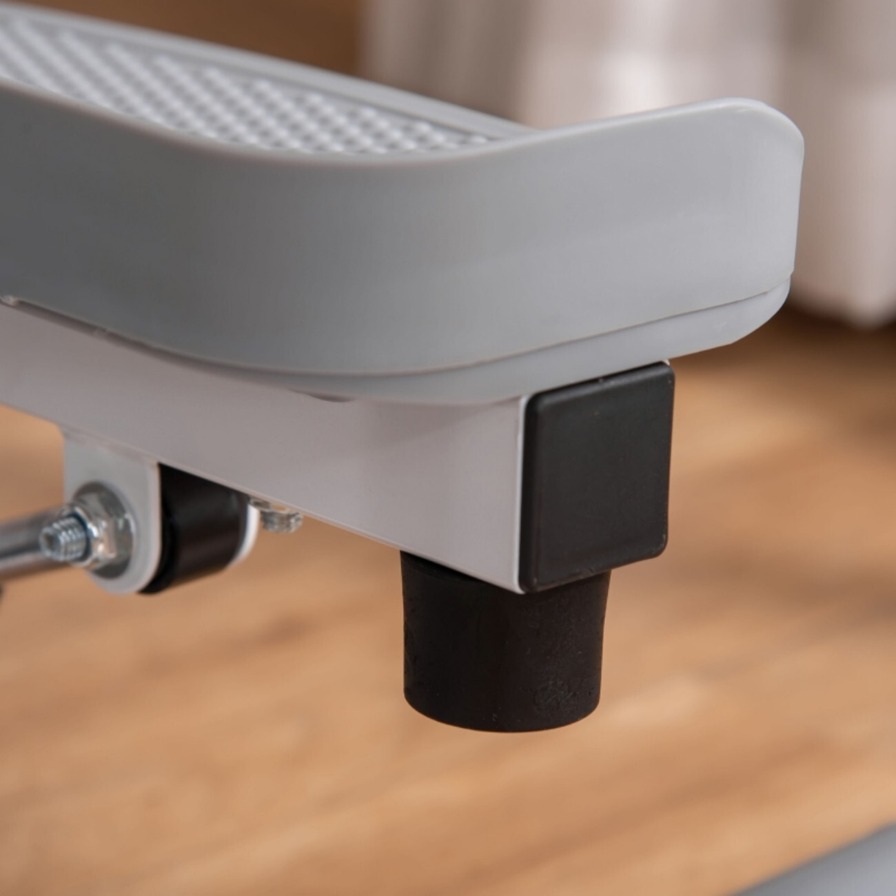 Zbliżenie szarej platformy schodkowej z czarną gumową stopką na drewnianej podłodze.