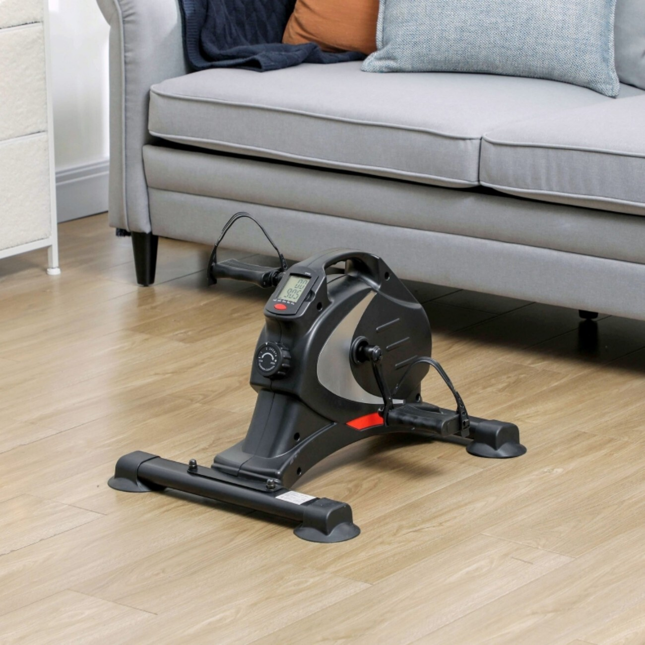 Czarny rower stacjonarny na drewnianej podłodze obok szarej kanapy.