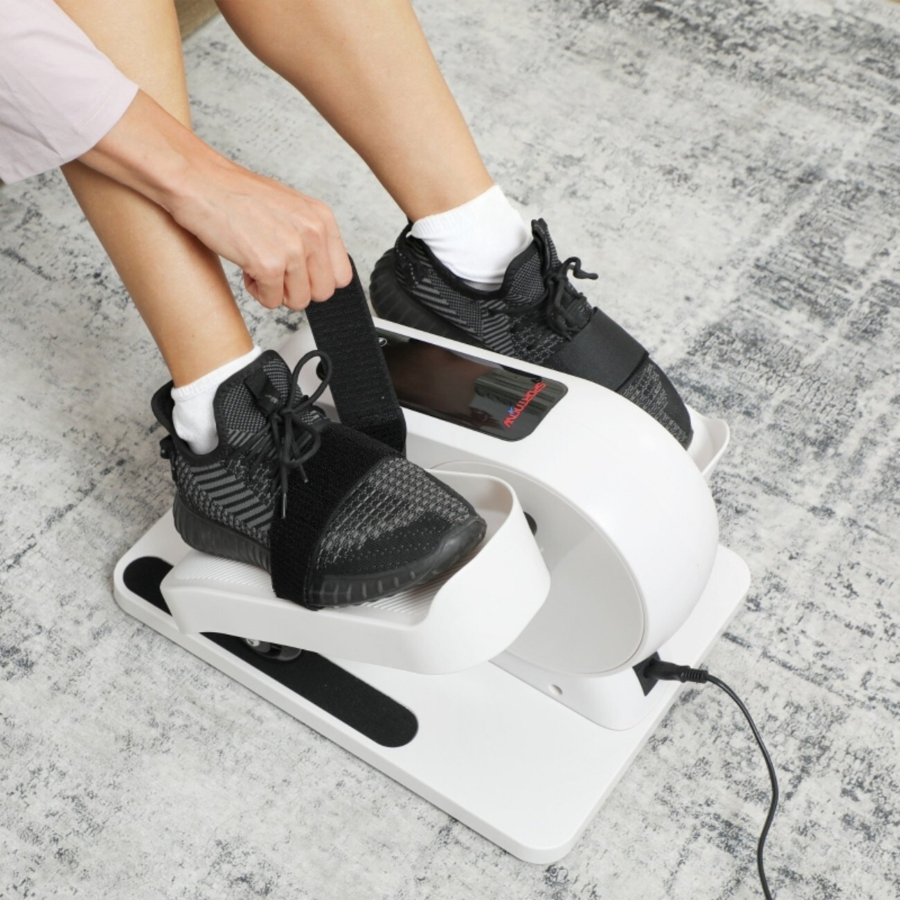 Osoba w czarnych butach sportowych na białej domowej maszynie treningowej.