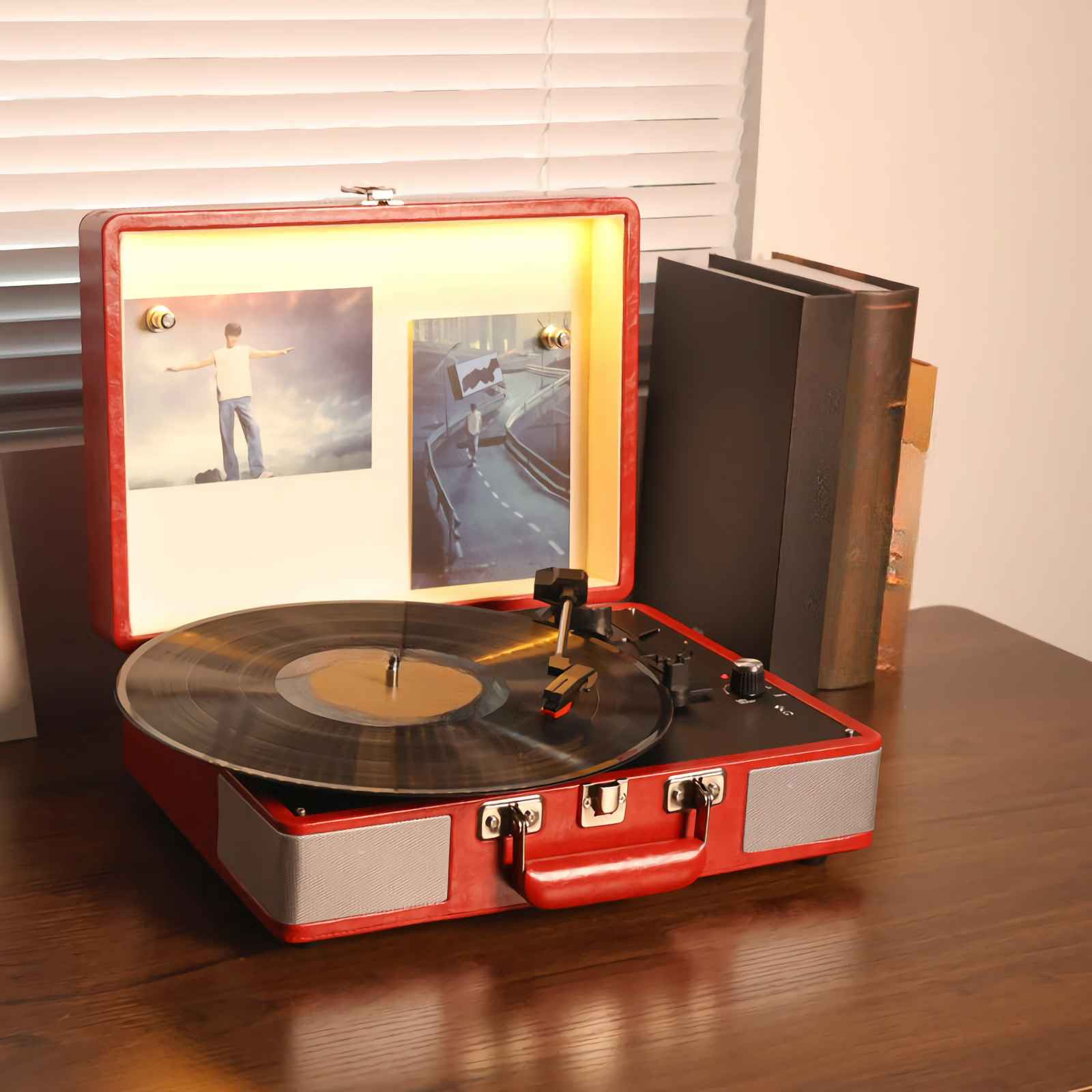 Ein rotes Plattenspieler mit Vinylplatte und zwei Bildern steht auf einem Holztisch.
