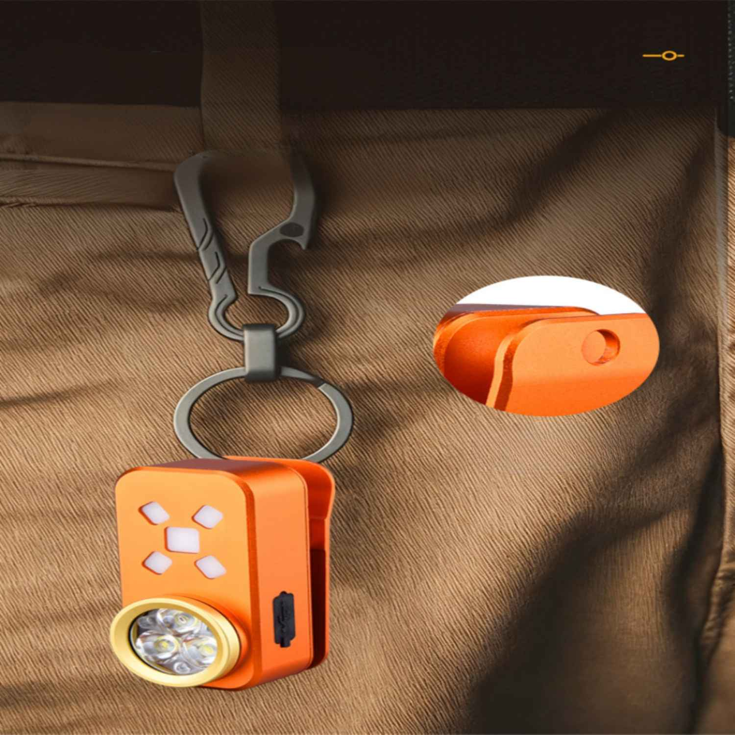 Eine orangefarbene Schlüsselanhänger-Taschenlampe mit Metallclip hängt an brauner Kleidung.