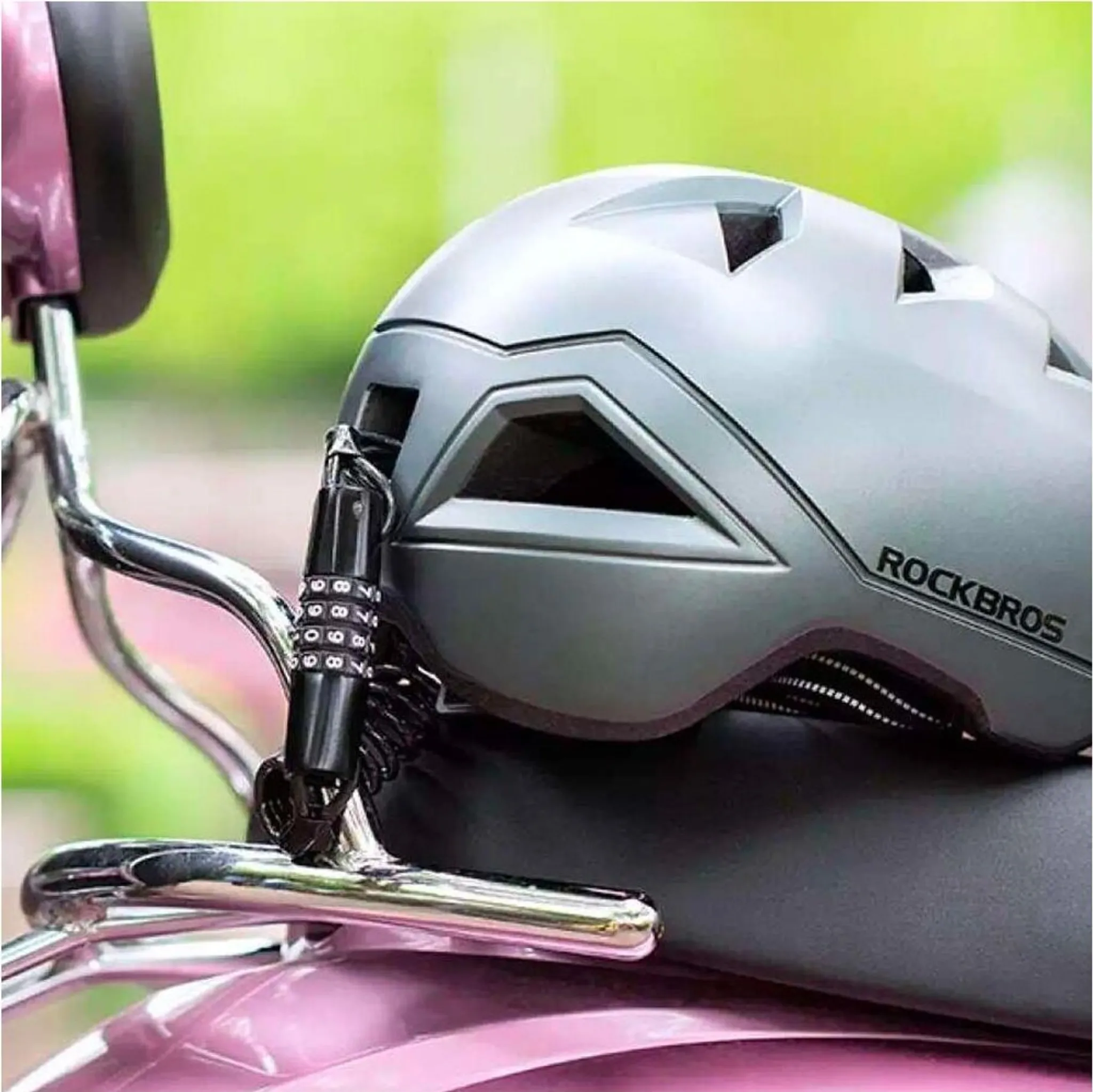 Ein silberner Fahrradhelm mit Zahlenschloss auf einem pinken Roller.