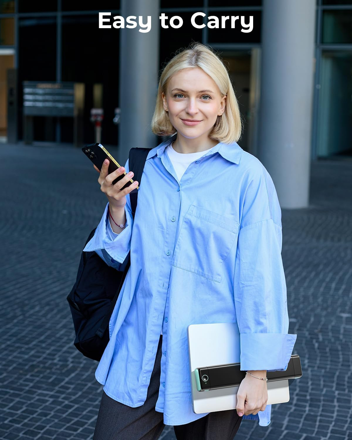Une femme blonde en chemise bleue tient un téléphone et un ordinateur portable.