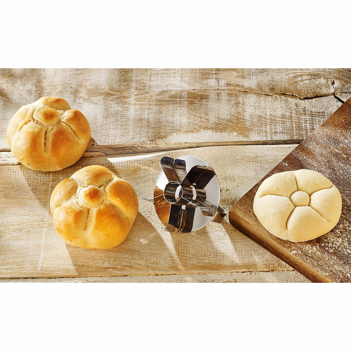 Zwei gebackene Brötchen, ein Ausstecher und ein Teigbrötchen auf Holz.