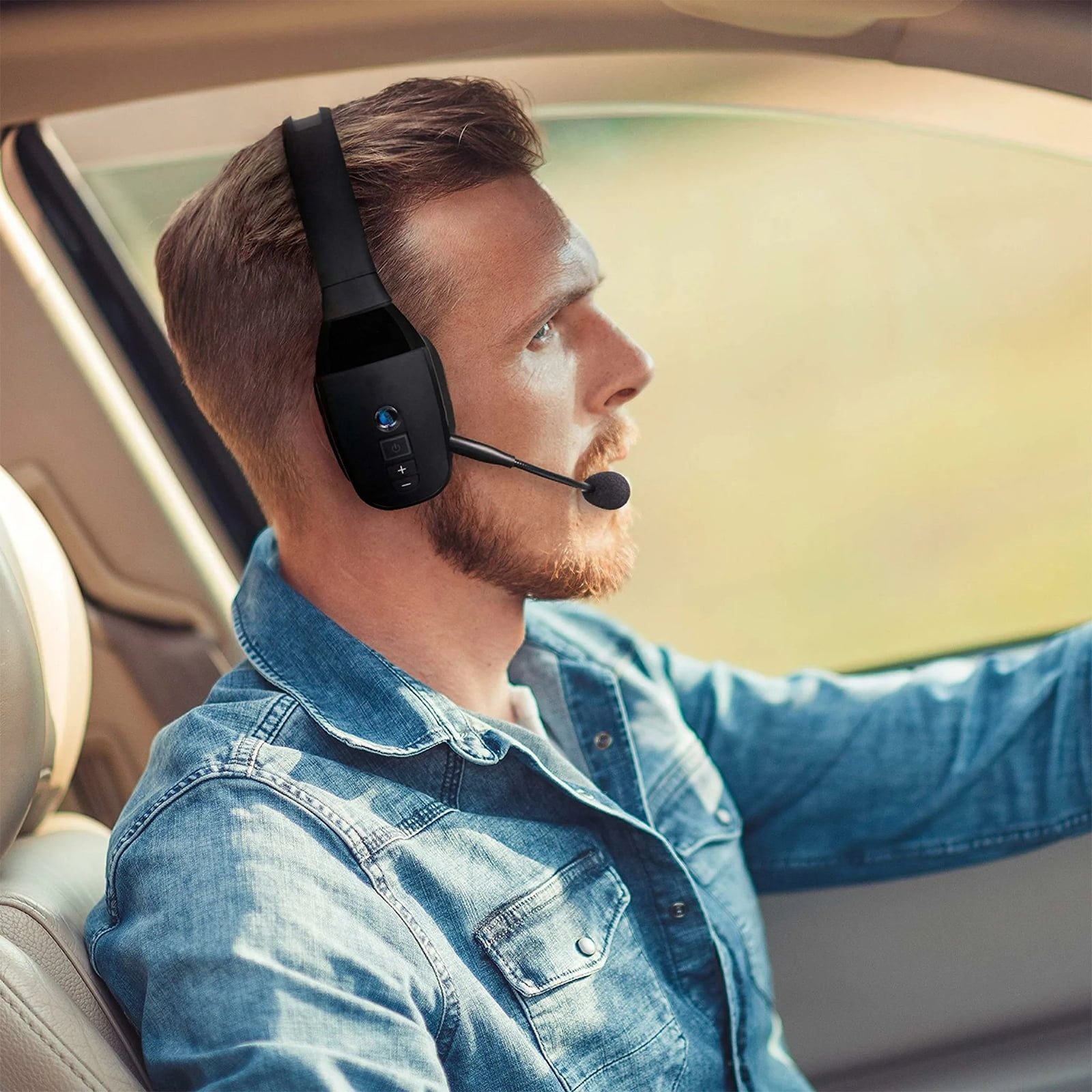 Mann mit Headset fährt Auto, trägt Jeanshemd. Draußen unscharf.