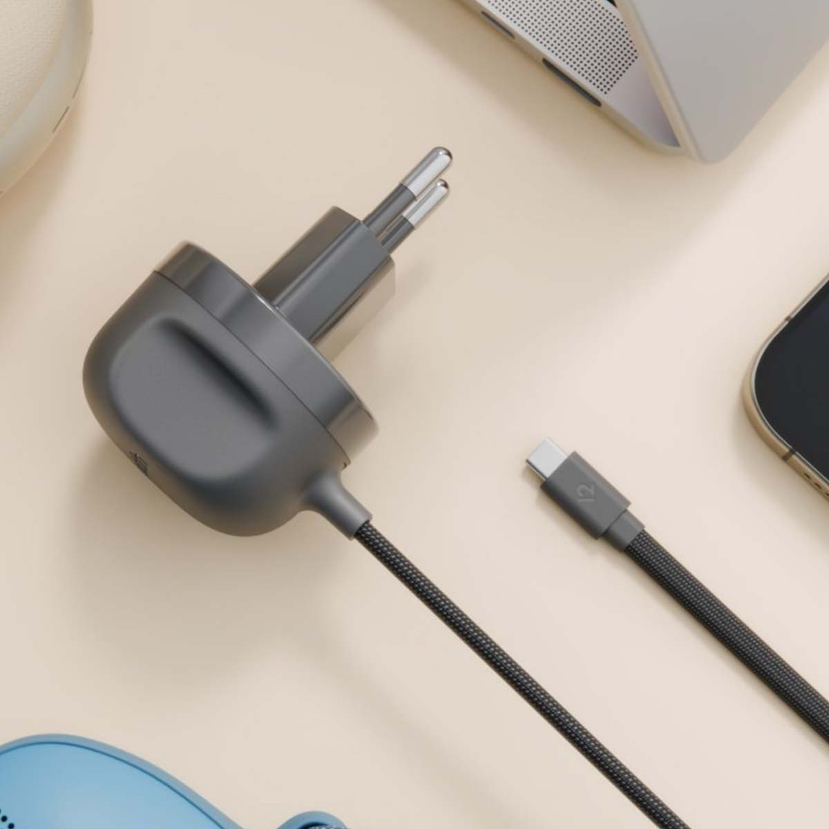 Un alimentatore grigio con cavo USB-C, laptop e telefono su sfondo crema.
