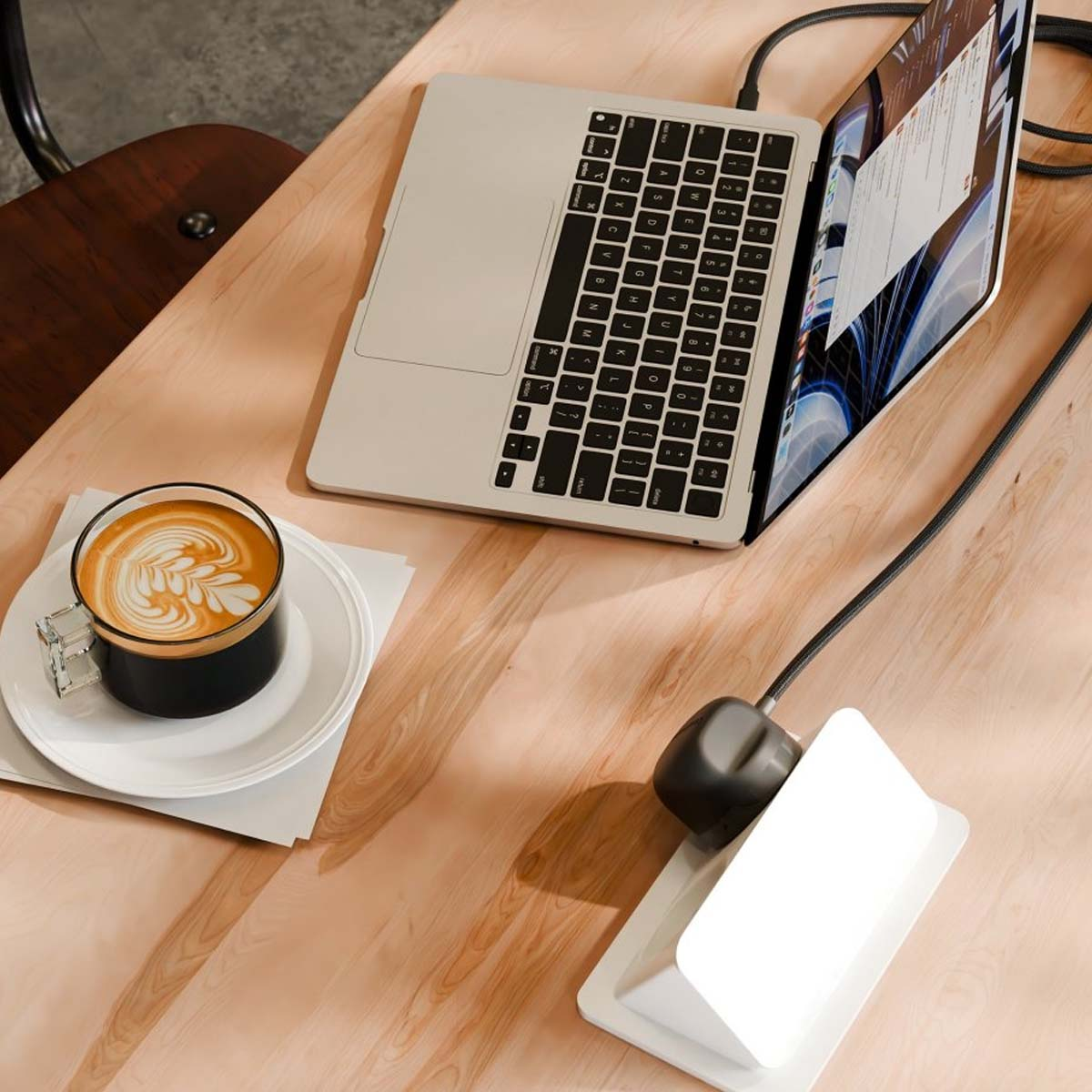 Laptop con caffè e caricabatterie su scrivania in legno.