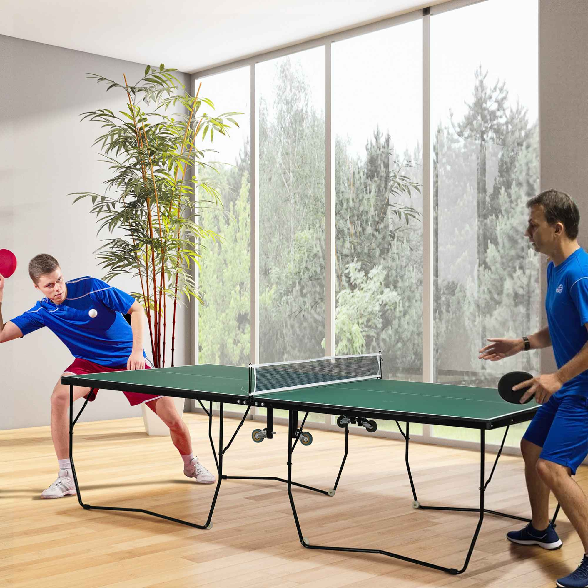 Zwei Männer spielen Tischtennis in einem Raum mit großen Fenstern und einer Bambuspflanze.