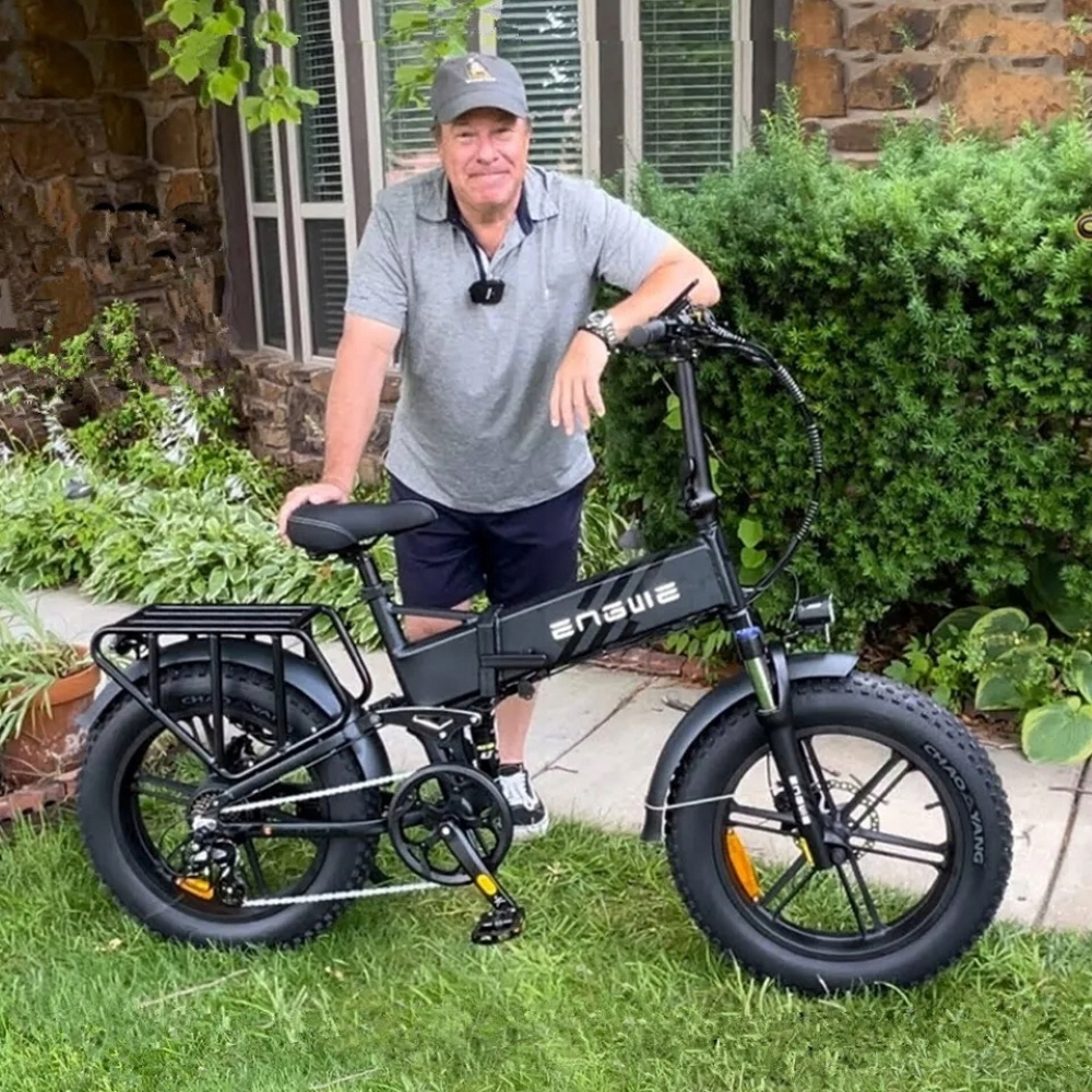 Un uomo in polo grigia è accanto a una bici elettrica nera all'aperto.
