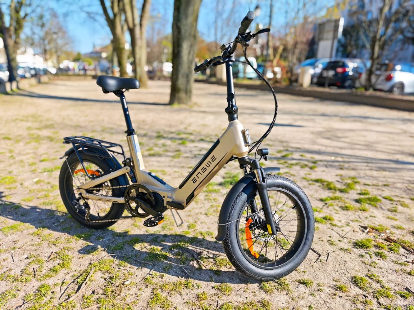 Una e-bike pieghevole beige è parcheggiata all'aperto su terra ed erba.