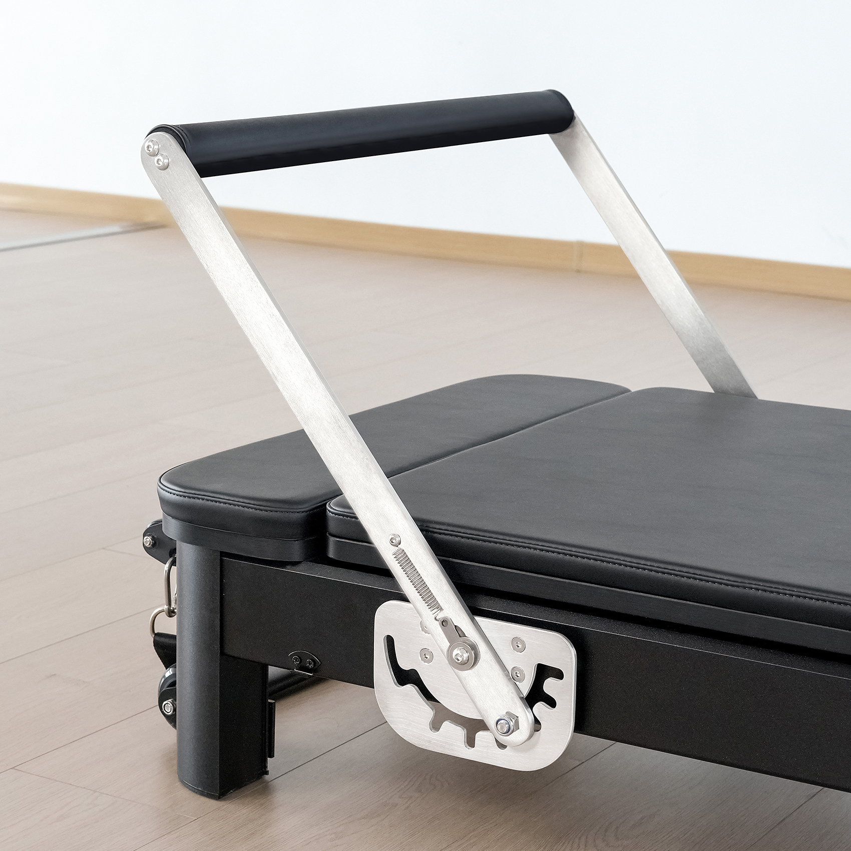 Ein schwarzer Pilates-Reformer mit silbernen Griffen und Holzfußboden.
