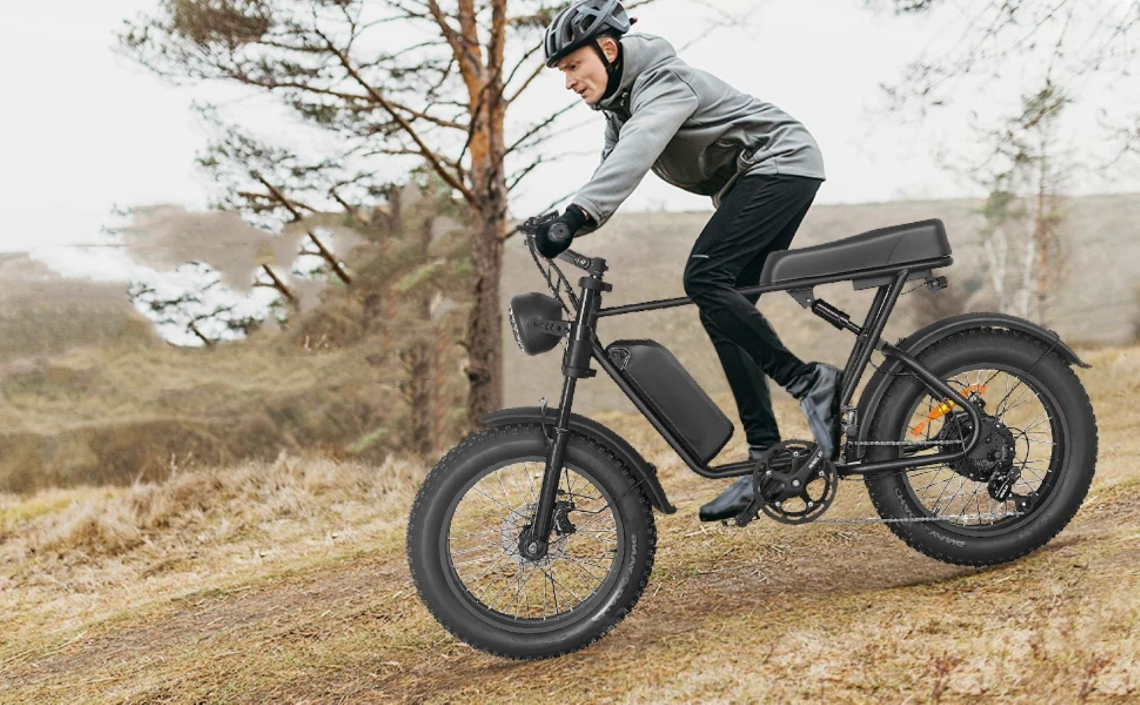 Un hombre monta una bicicleta eléctrica negra por un camino de tierra con árboles.