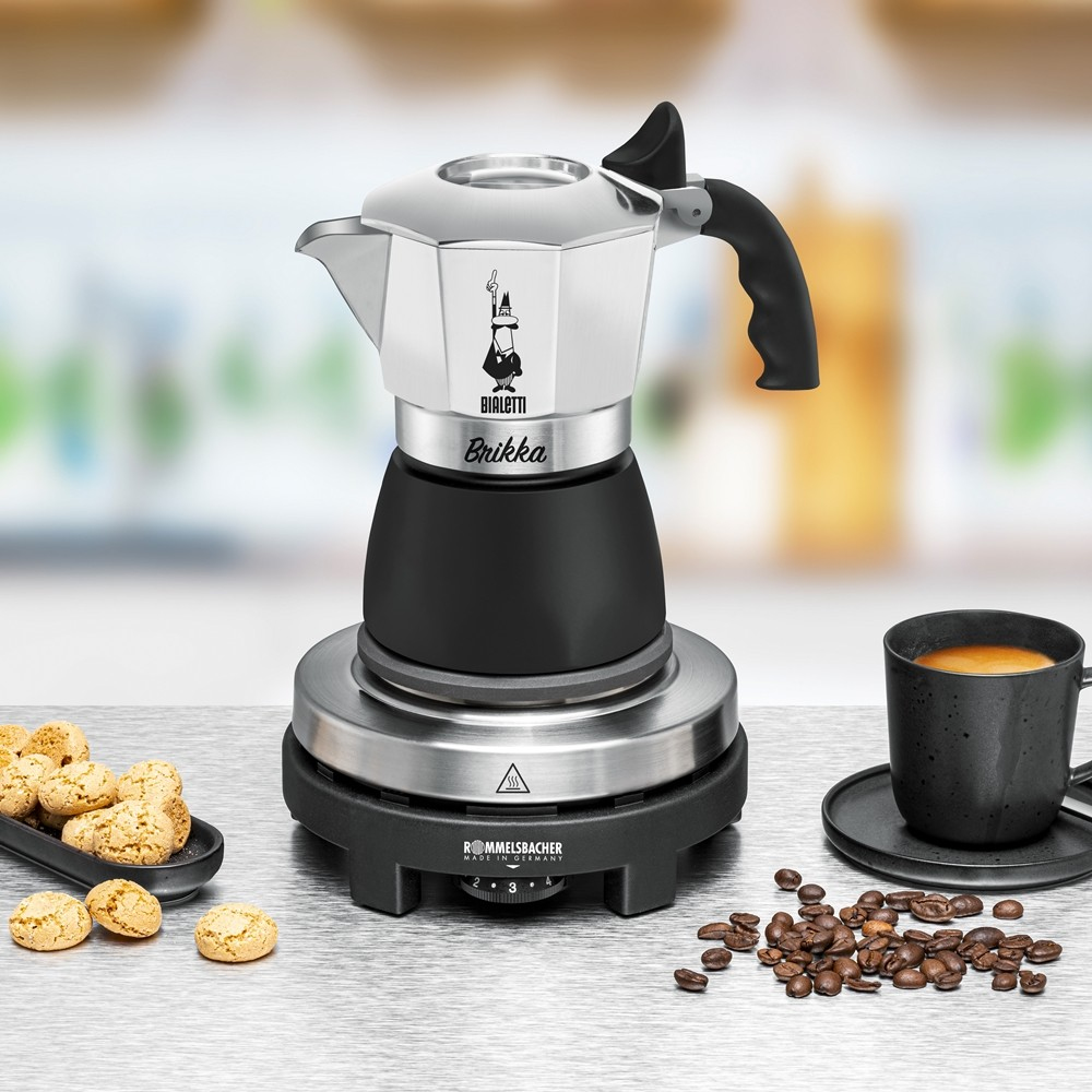Eine Bialetti Espressokanne auf einer Heizplatte mit Kaffee, Keksen und Bohnen.