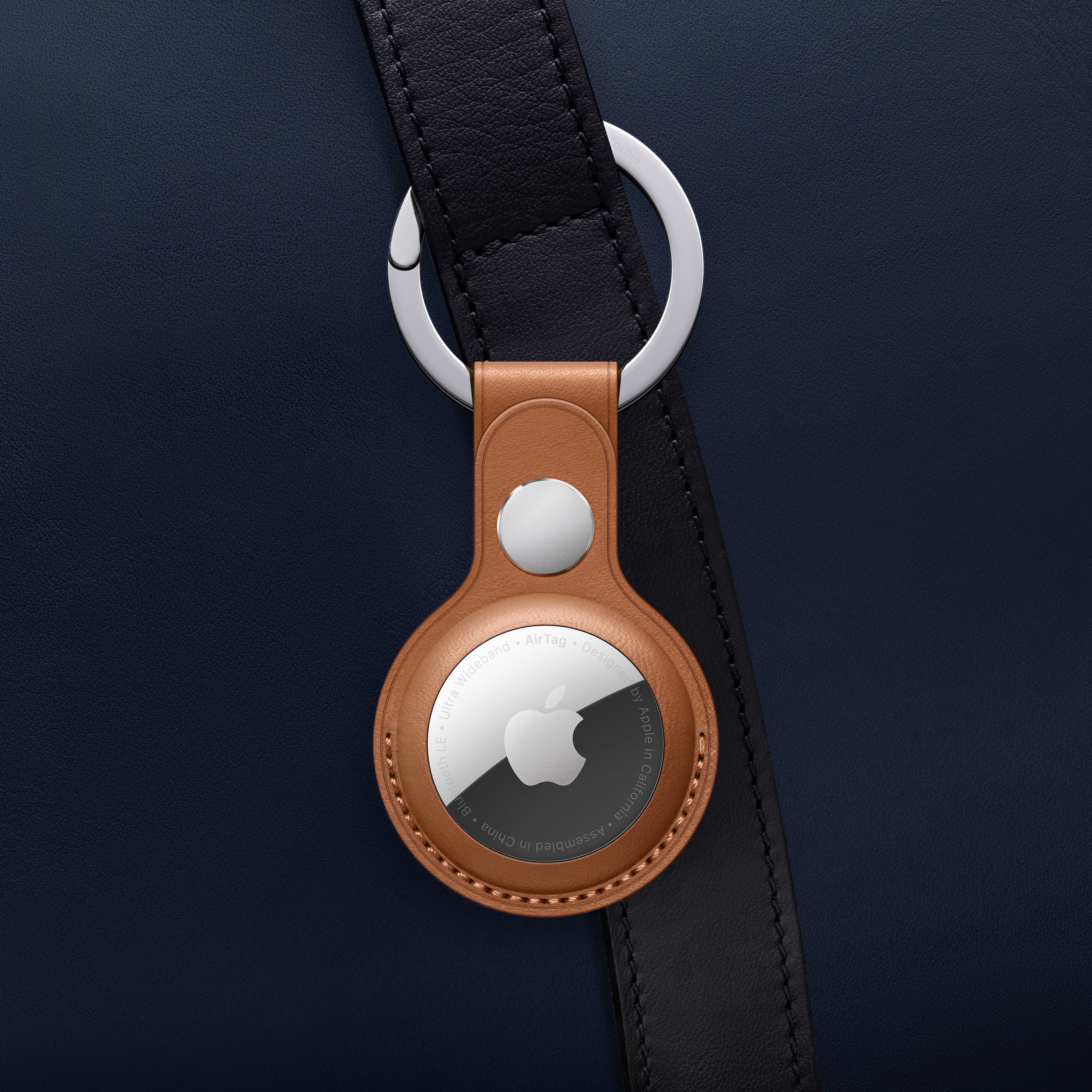 Bruine lederen hoes met een Apple AirTag en zilveren ring op een donkerblauwe achtergrond.