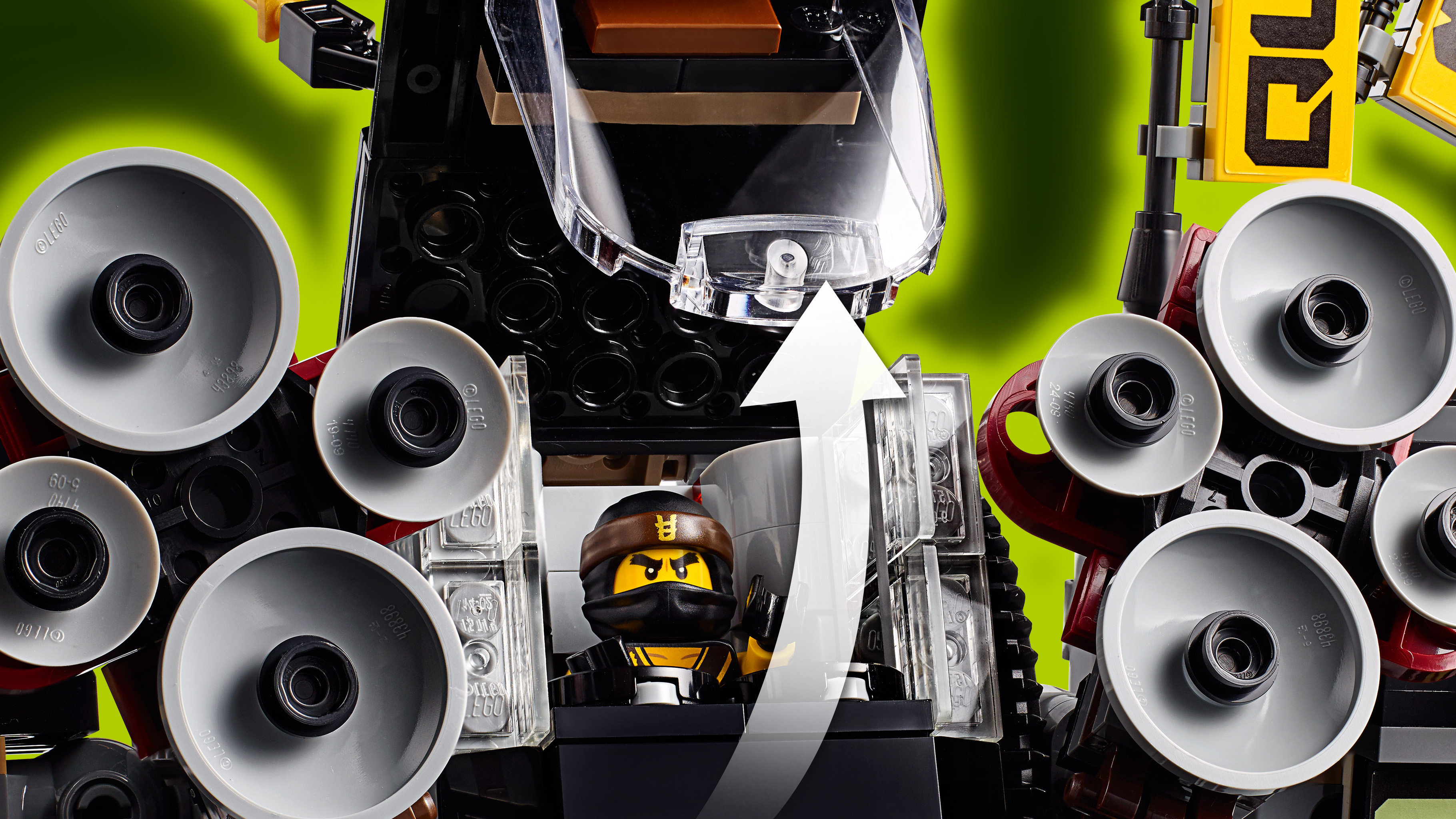 Ninja Lego siedzi w pojeździe Lego z dużymi szarymi kołami i przezroczystymi elementami.