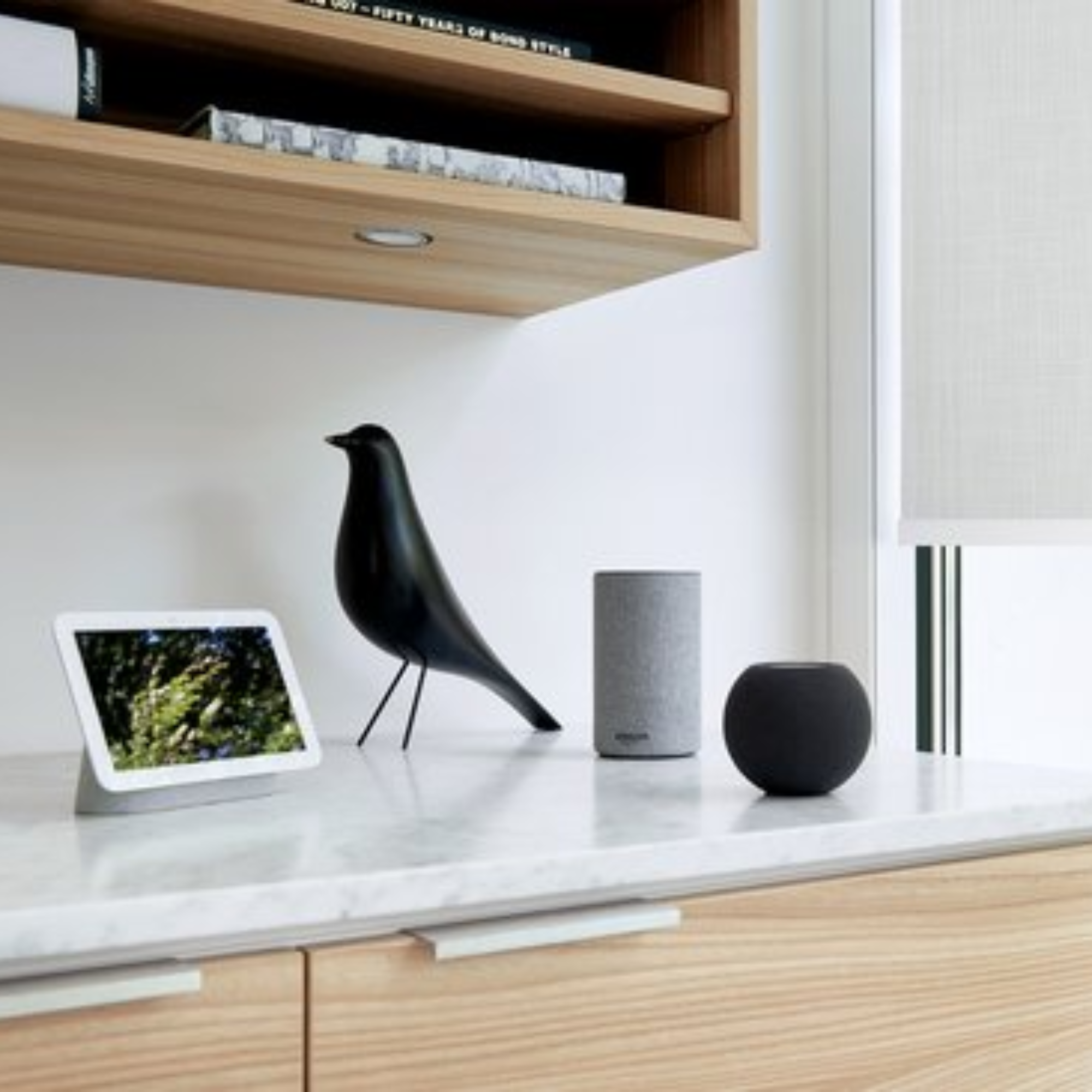 Een zwarte vogel op een plank naast een smart speaker en tablet.