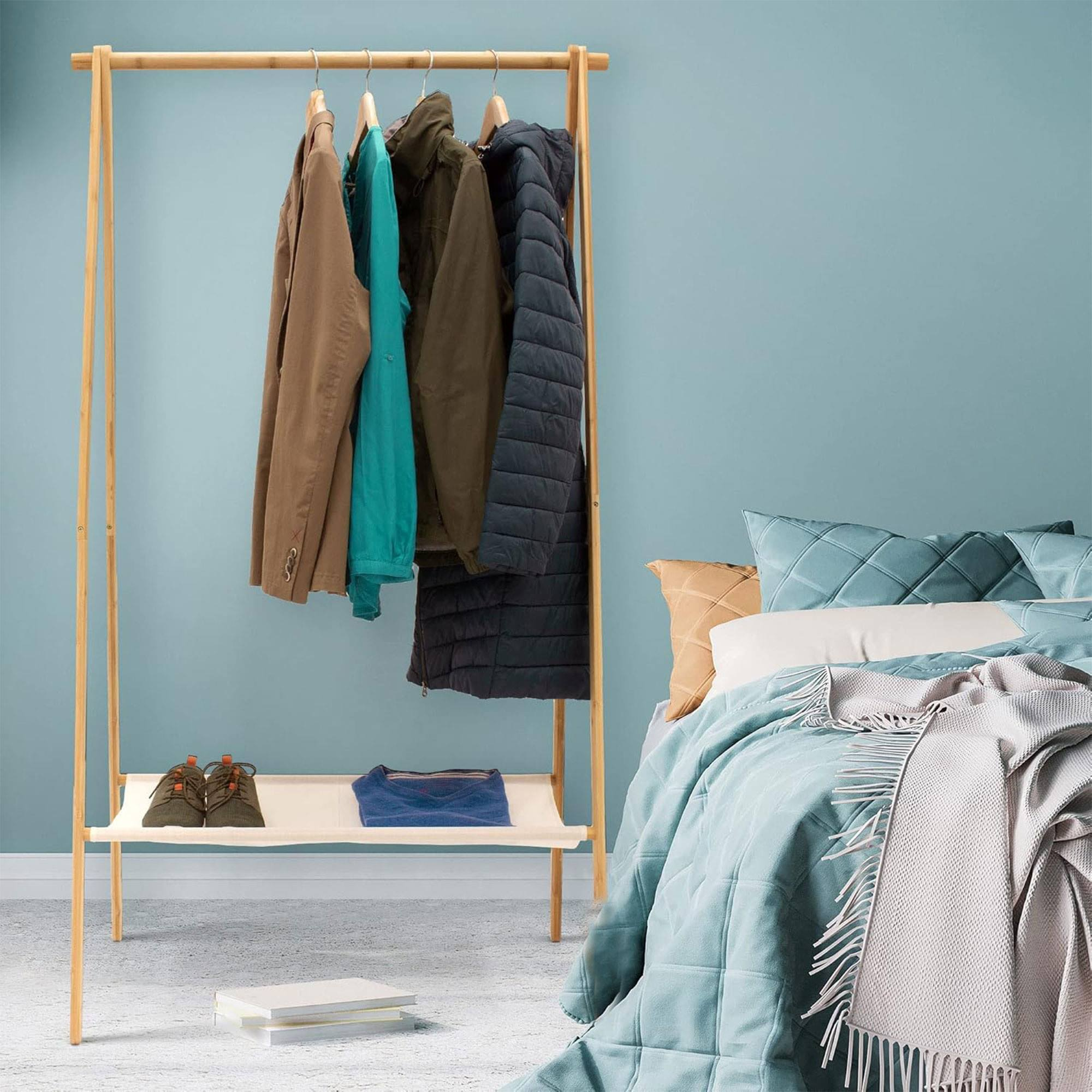 Perchero de madera con ropa, zapatos y cama al fondo.