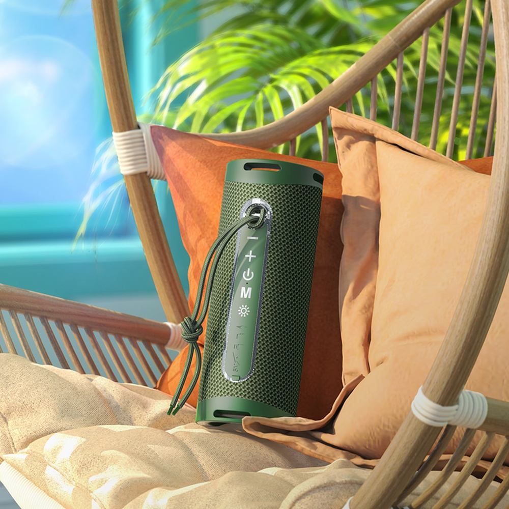 Altavoz verde en silla de mimbre con cojines, palmeras al fondo.
