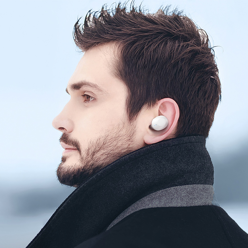Uomo con auricolare bianco e cappotto scuro all'aperto.