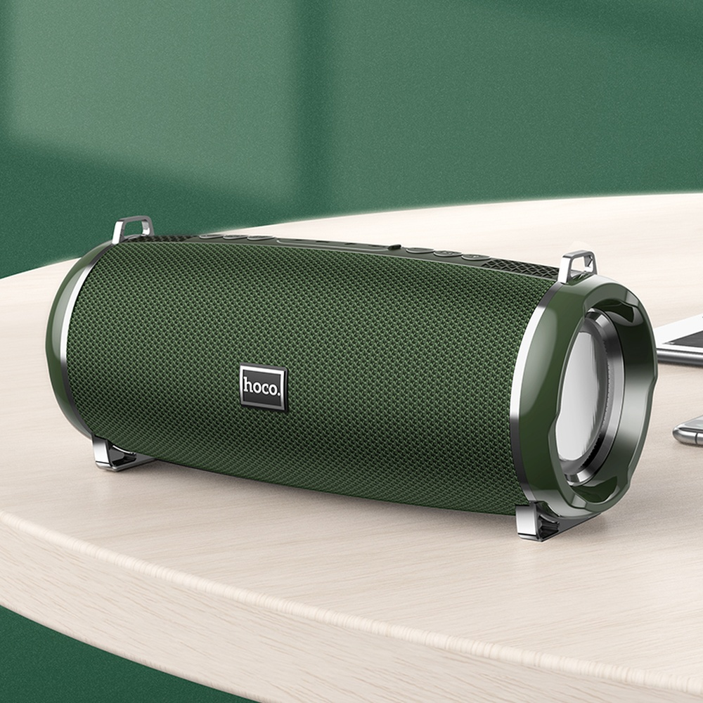 Altavoz Hoco verde con detalles plateados sobre una mesa de madera.