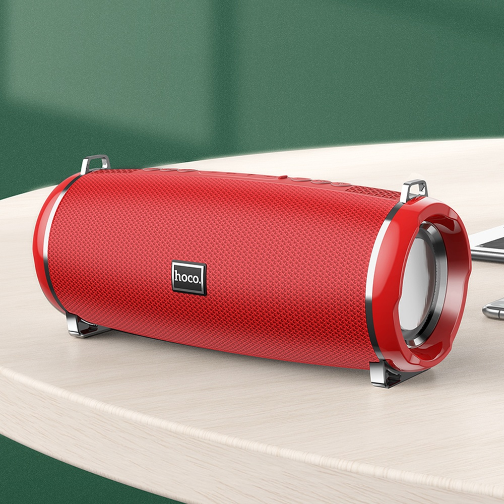 Altavoz portátil rojo hoco. con detalles plateados sobre mesa de madera clara.