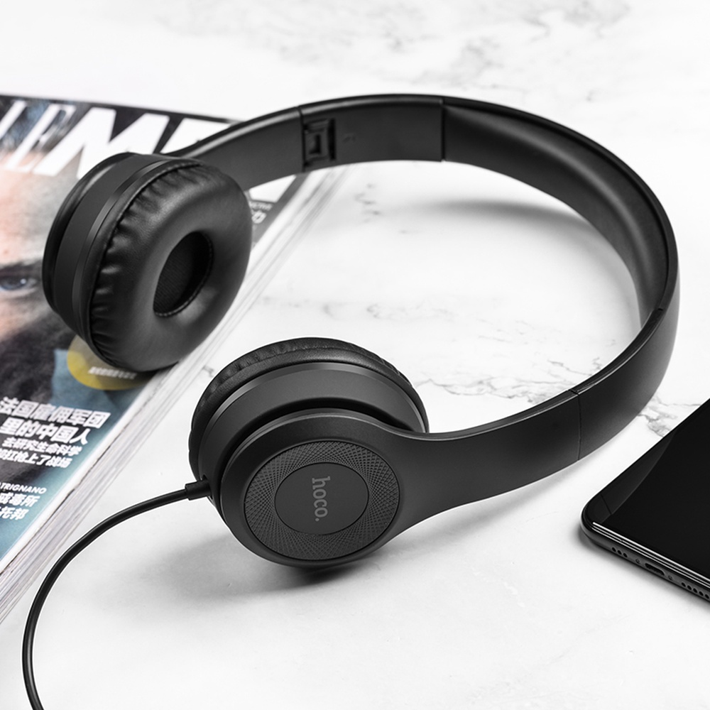 Cuffie nere su superficie in marmo accanto a rivista e smartphone.