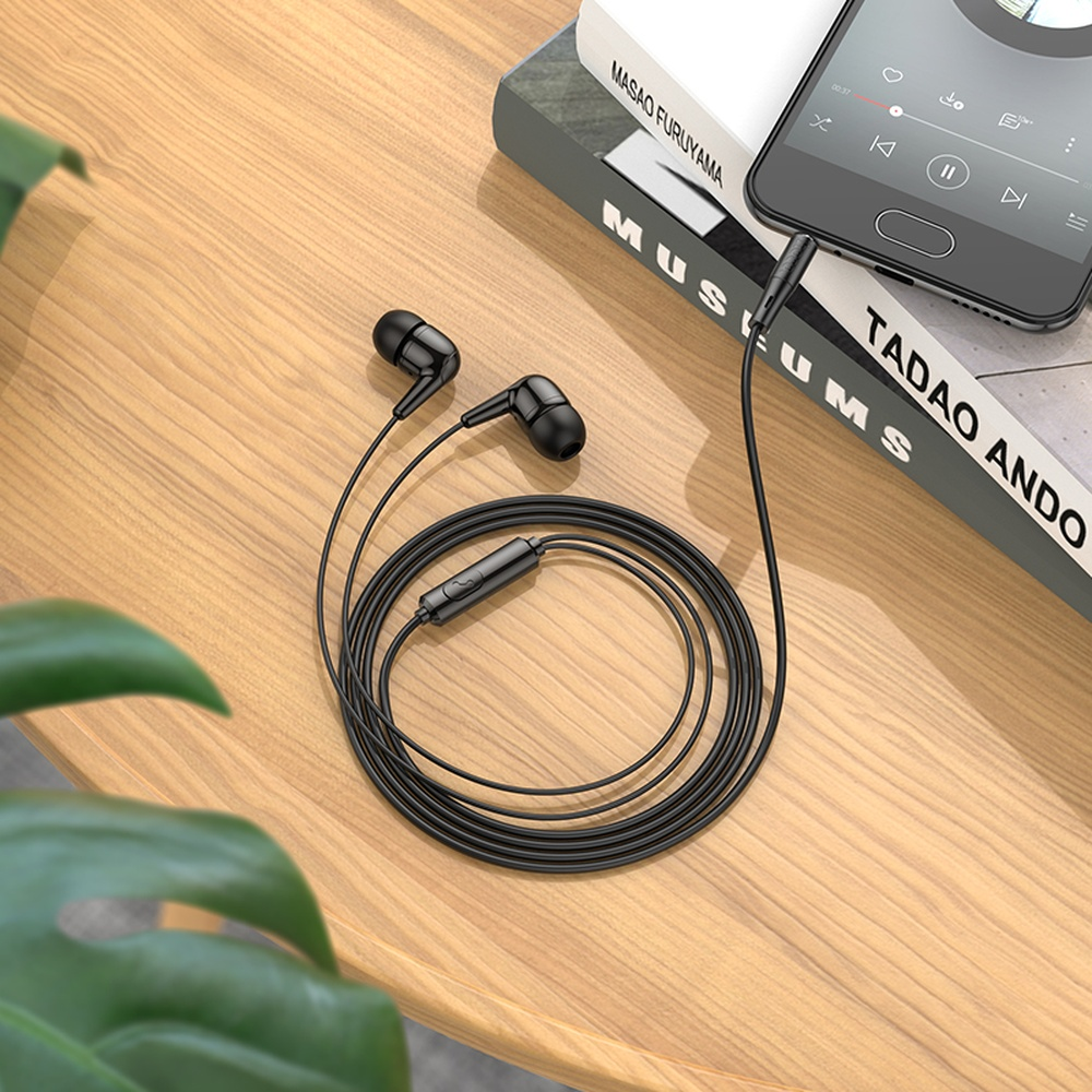 Auricolari neri con cavo appoggiati su un tavolo di legno accanto a libri e uno smartphone.