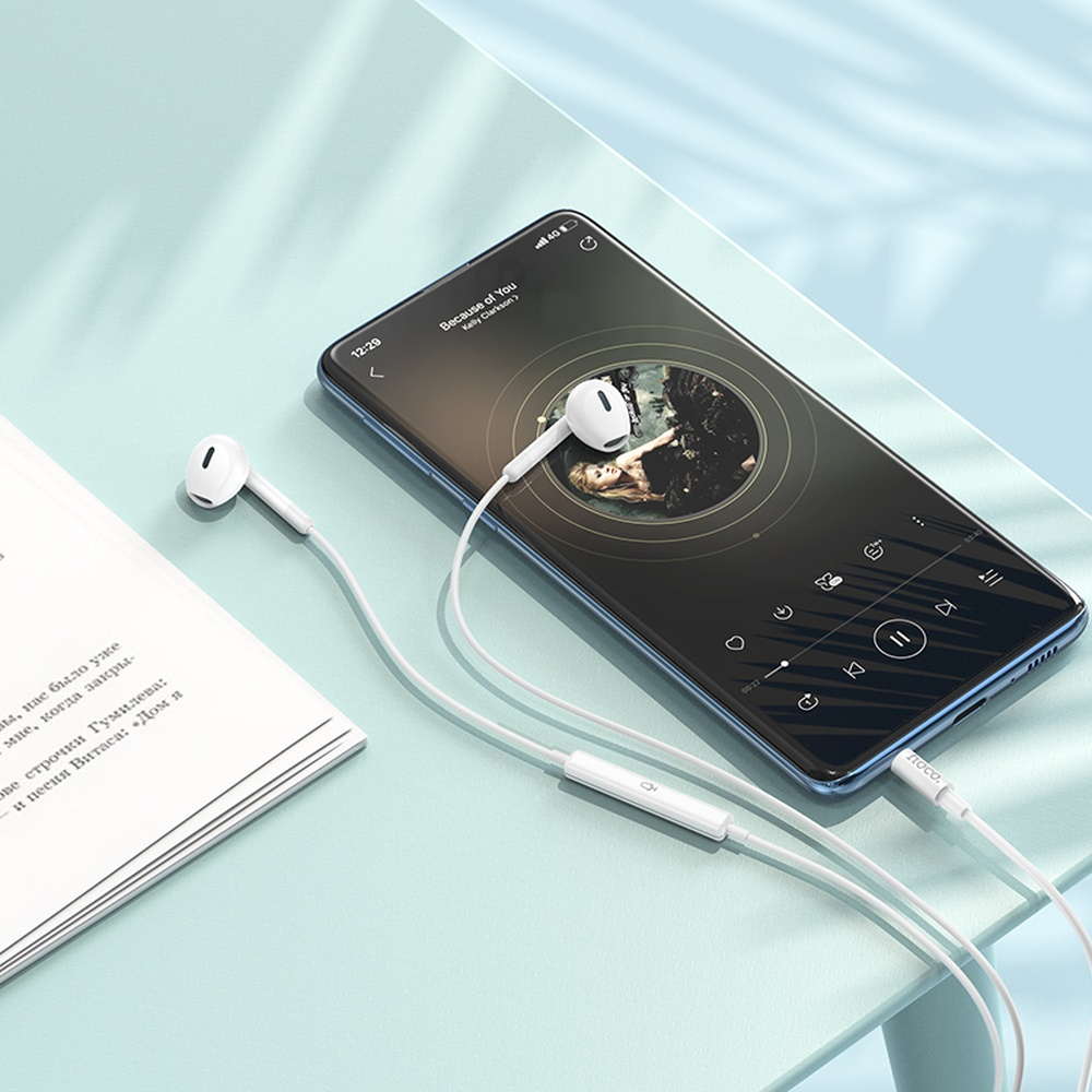 Auriculares blancos conectados a un smartphone reproduciendo música, junto a un libro.