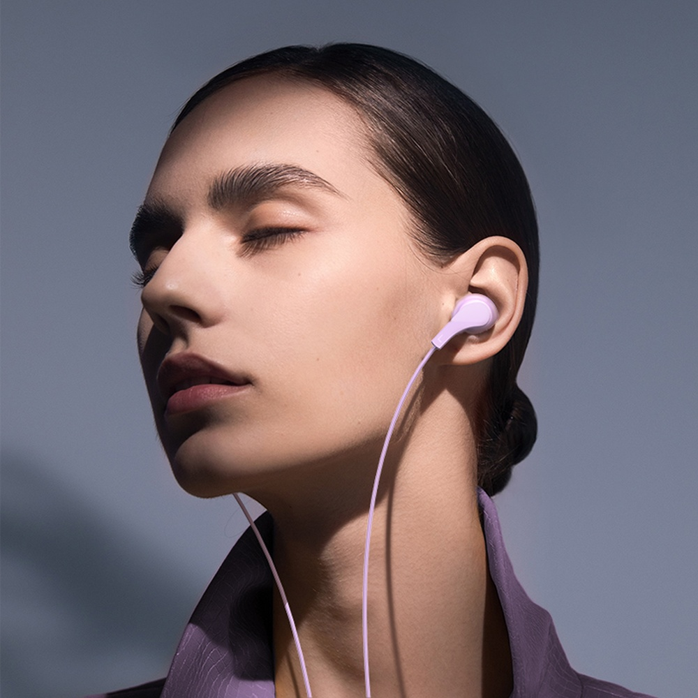 Mujer con ojos cerrados usa auriculares morados, en sombra.