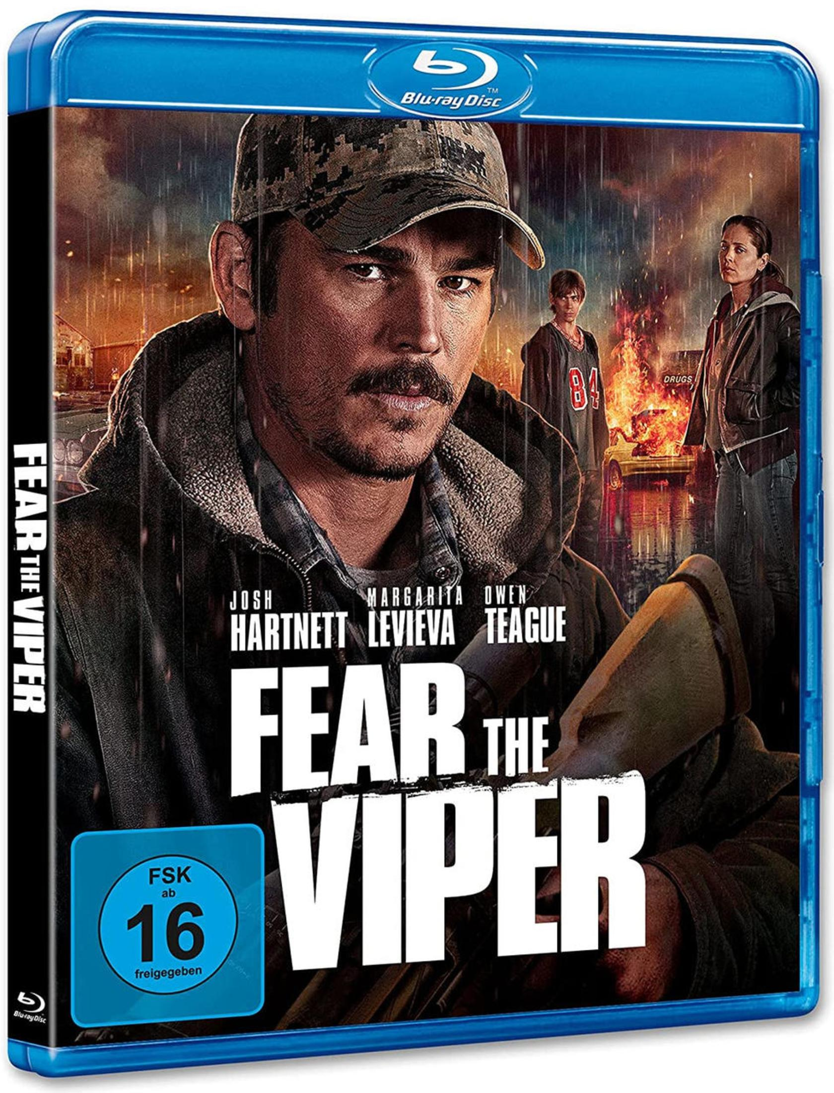 Ein Mann mit Tarnkappe im Regen, im Hintergrund brennendes Auto. Filmplakat.