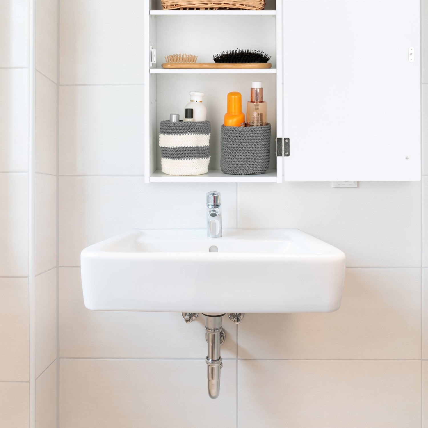 Un lavabo blanco con grifo cromado, encima un armario abierto con artículos de tocador.