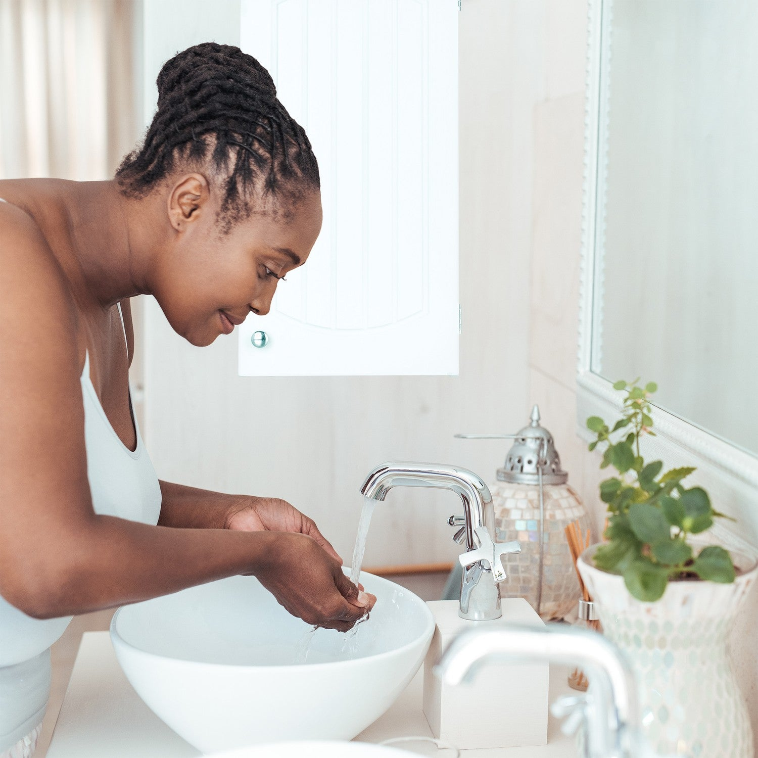 Mujer lavándose la cara con agua de un grifo en un baño.
