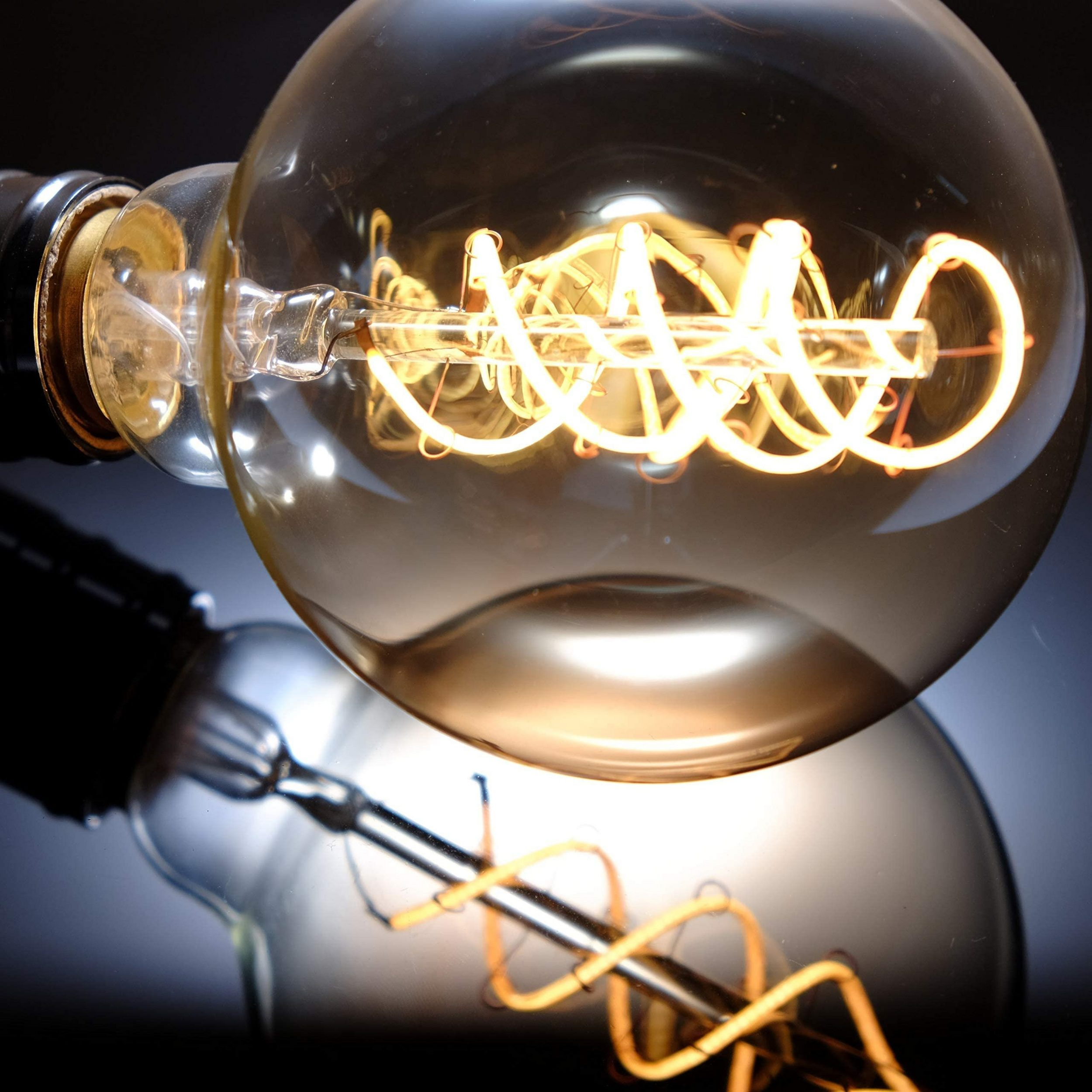 Bobina di filamento incandescente in una lampadina di vetro, riflessa su una superficie scura.