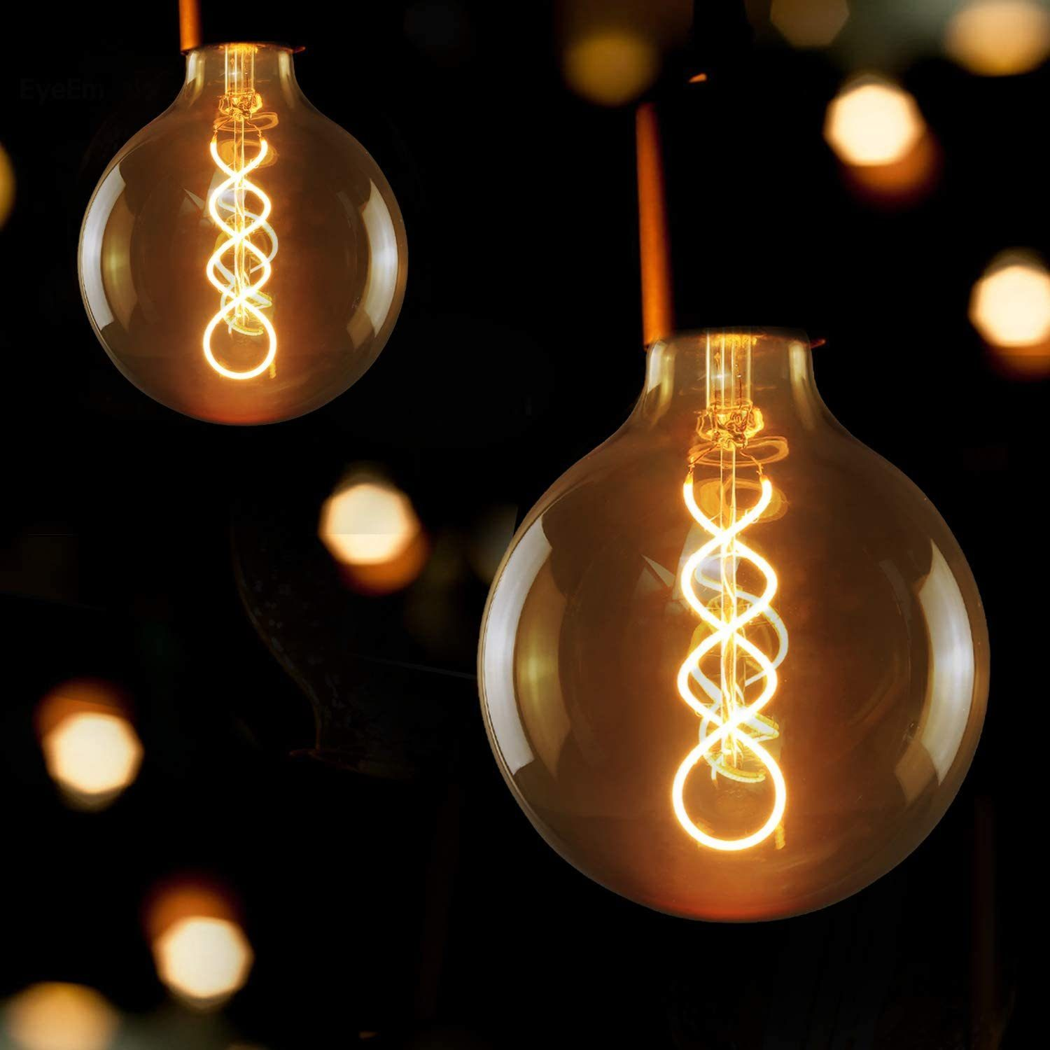 Due lampadine Edison con filamenti a spirale su sfondo scuro con luci.