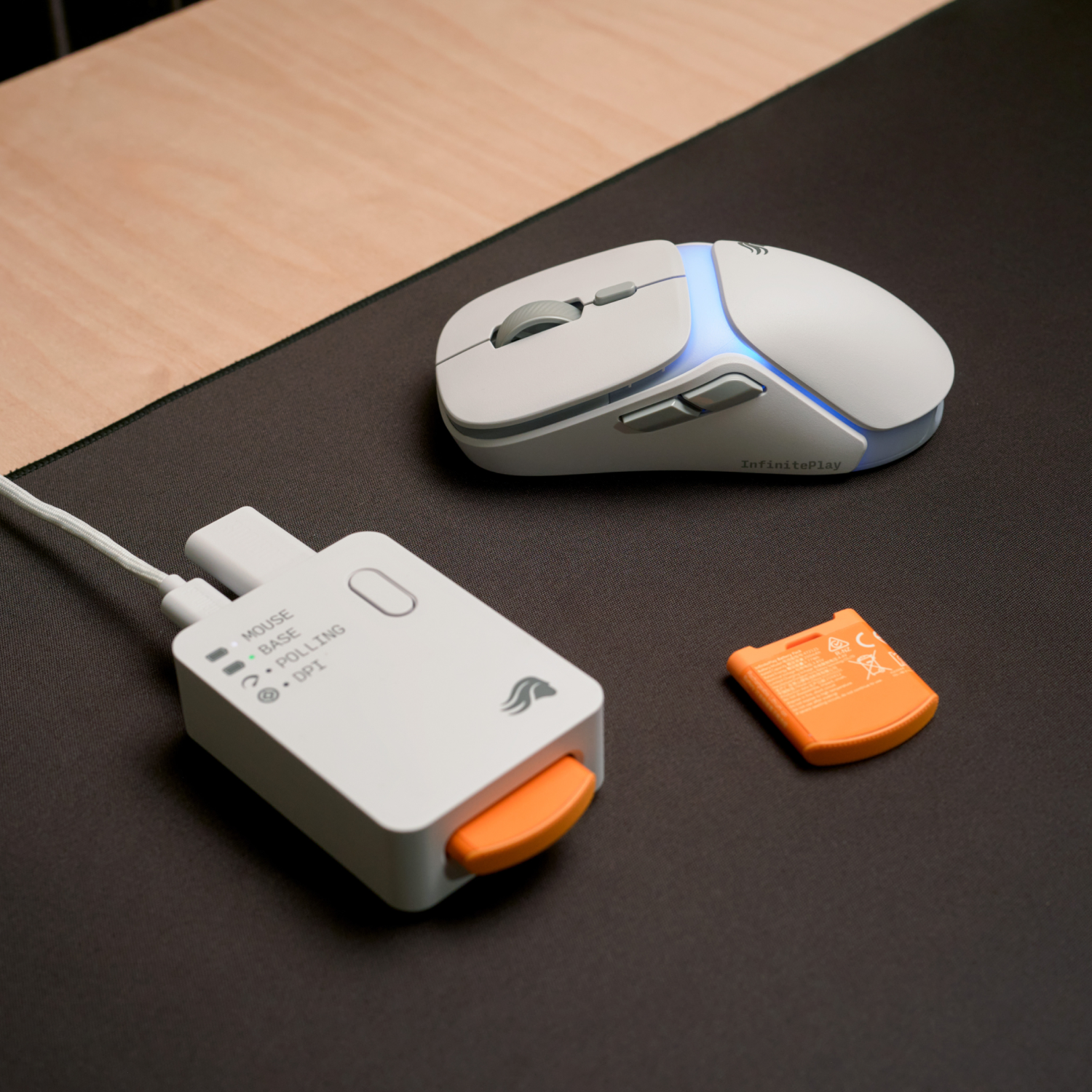 Mavi aydınlatmalı beyaz fare, dongle ve turuncu pil siyah mat üzerinde.