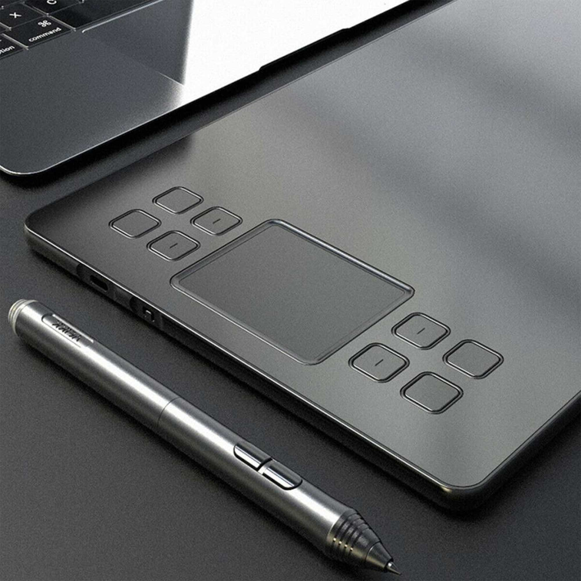 Gümüş renkli bir kalem, gri bir grafik tablet ve dizüstü bilgisayarın yanında duruyor.