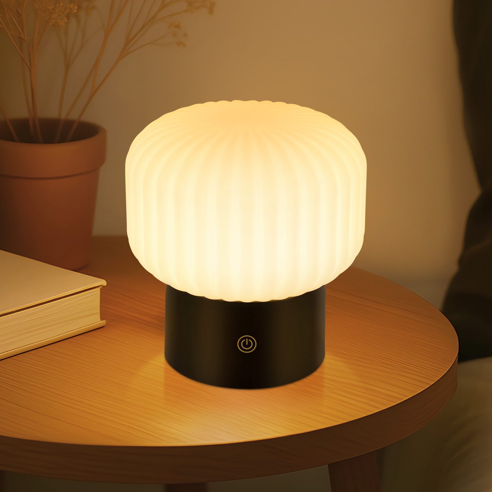 Una lampada a fungo illuminata su un tavolo di legno con libro e pianta.