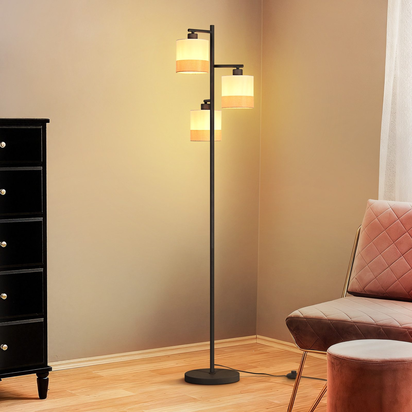 Una lampada da terra a tre bracci vicino a una cassettiera nera e una poltrona rosa.