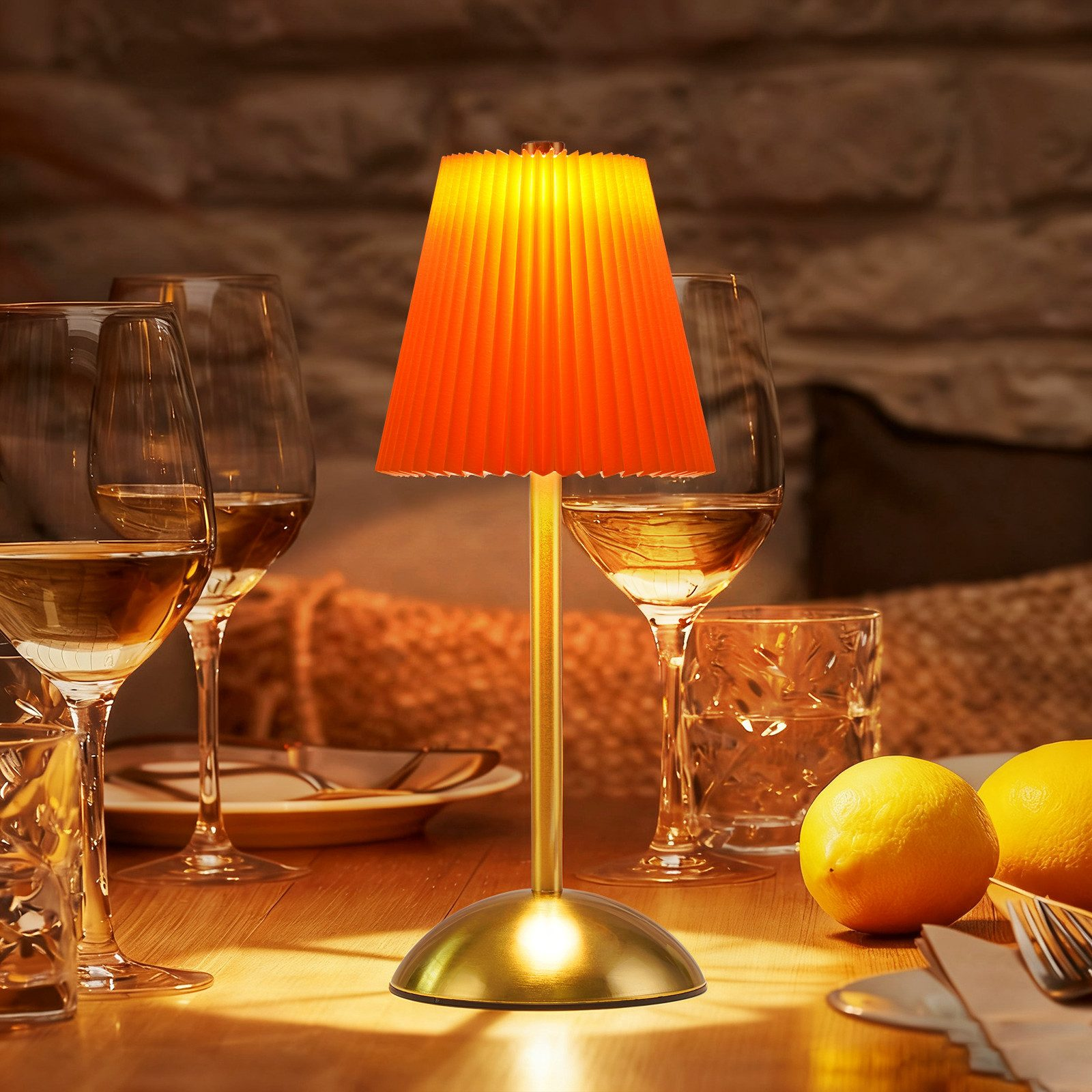 Un paralume arancione illumina un tavolo di legno con bicchieri e limoni.