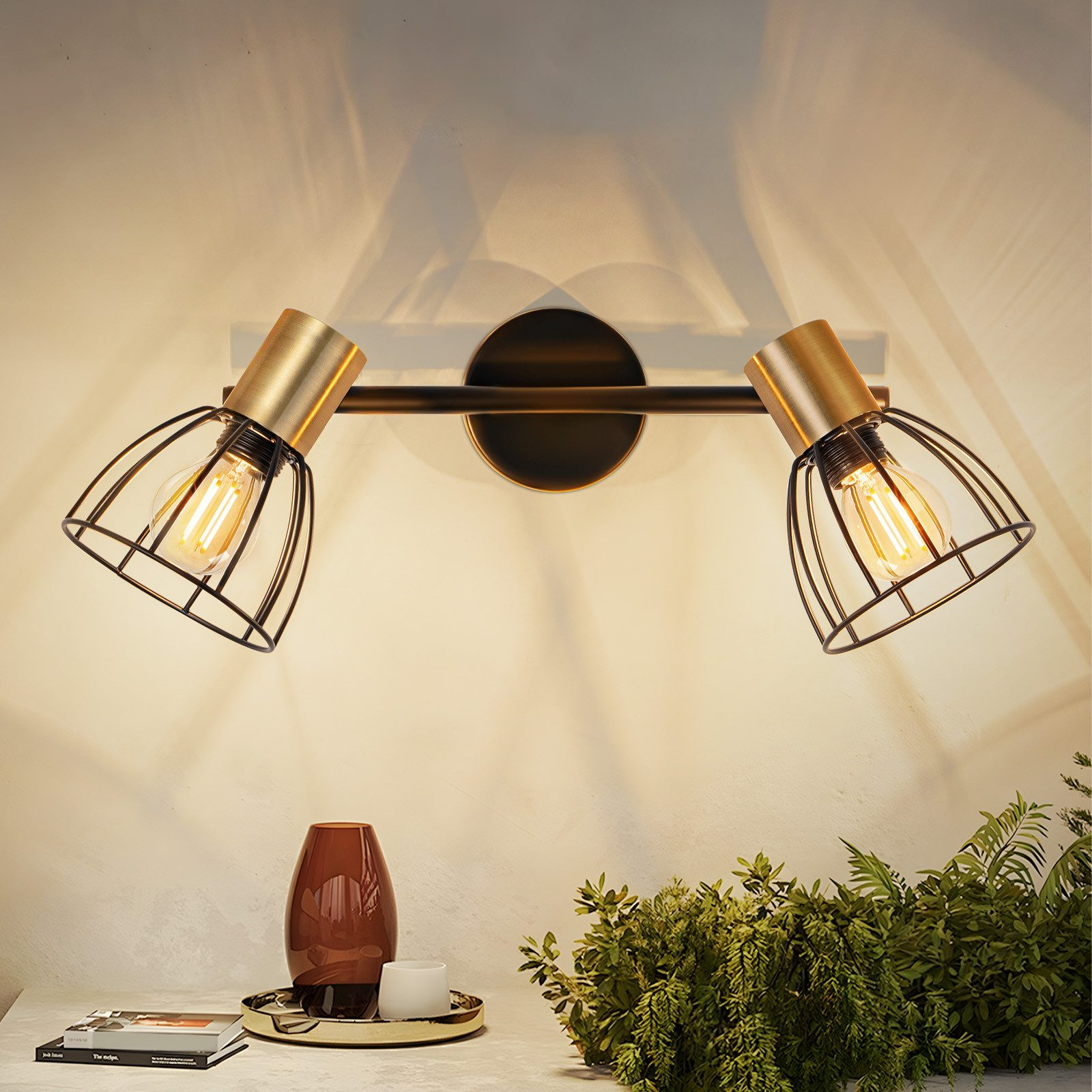 Una lampada da parete con due faretti dorati e gabbie in filo nero.