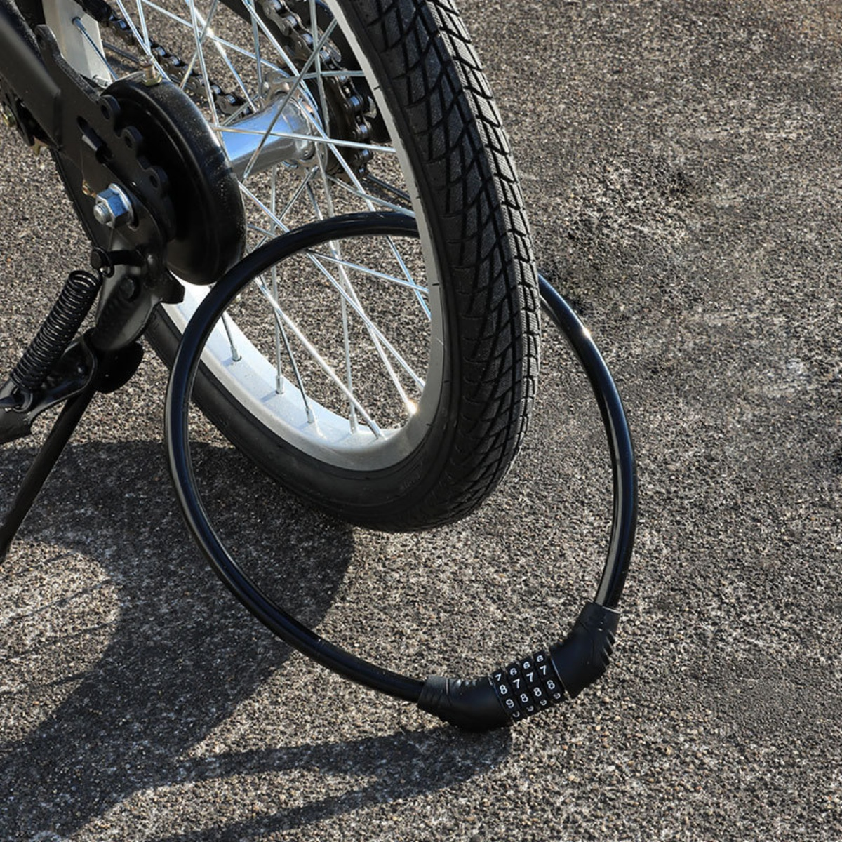 Ein schwarzes Fahrradschloss mit Zahlenkombination um das Hinterrad eines Fahrrads.