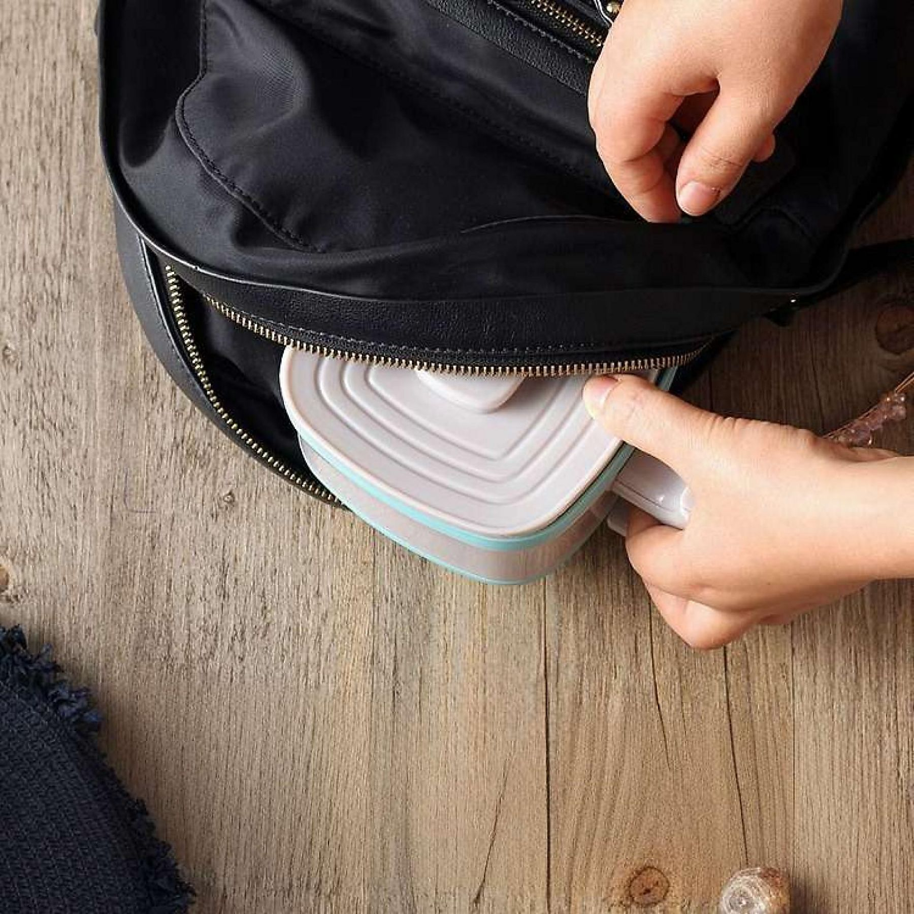 Eine Hand legt eine Herz-Lunchbox in einen schwarzen Rucksack.