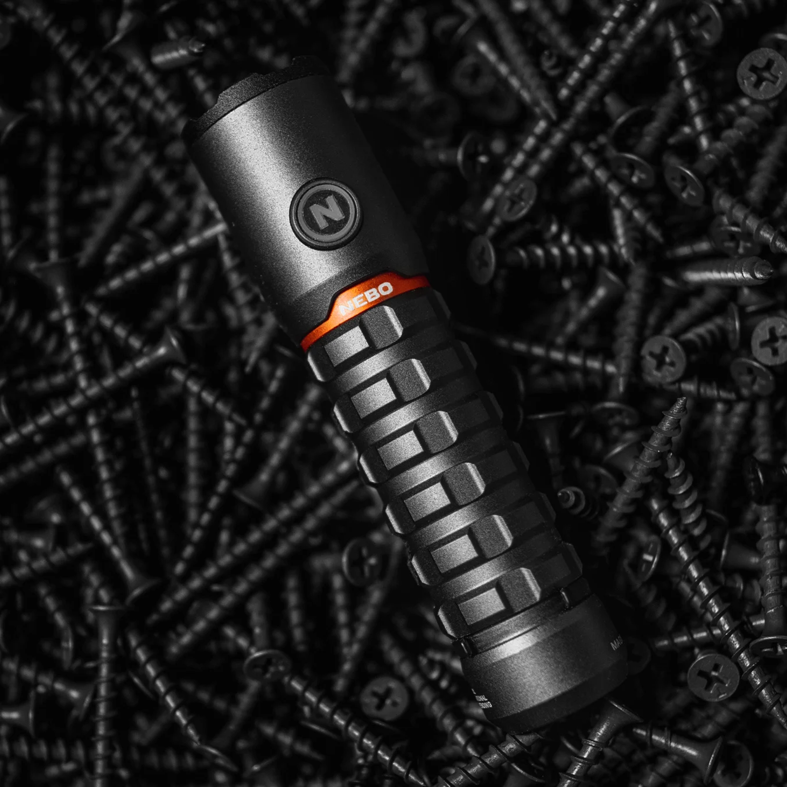 Une lampe de poche noire avec une bande orange repose sur de nombreuses vis noires.